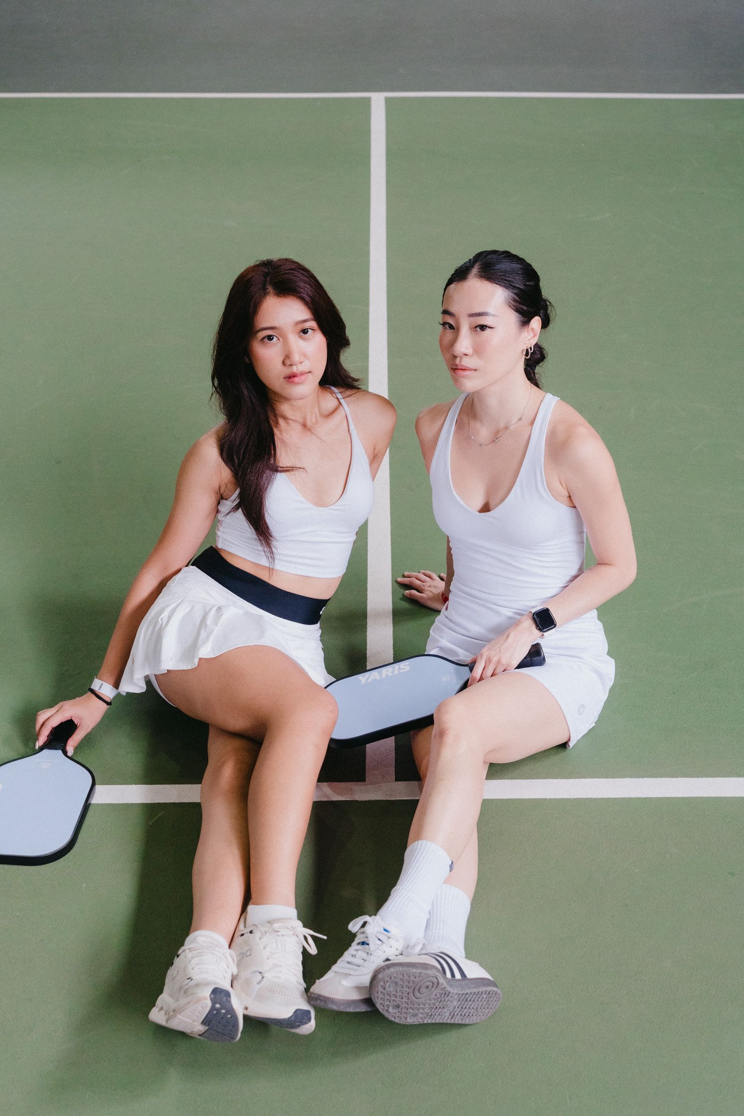 Two tennis players in white outfits taking a break and sitting on a green court.