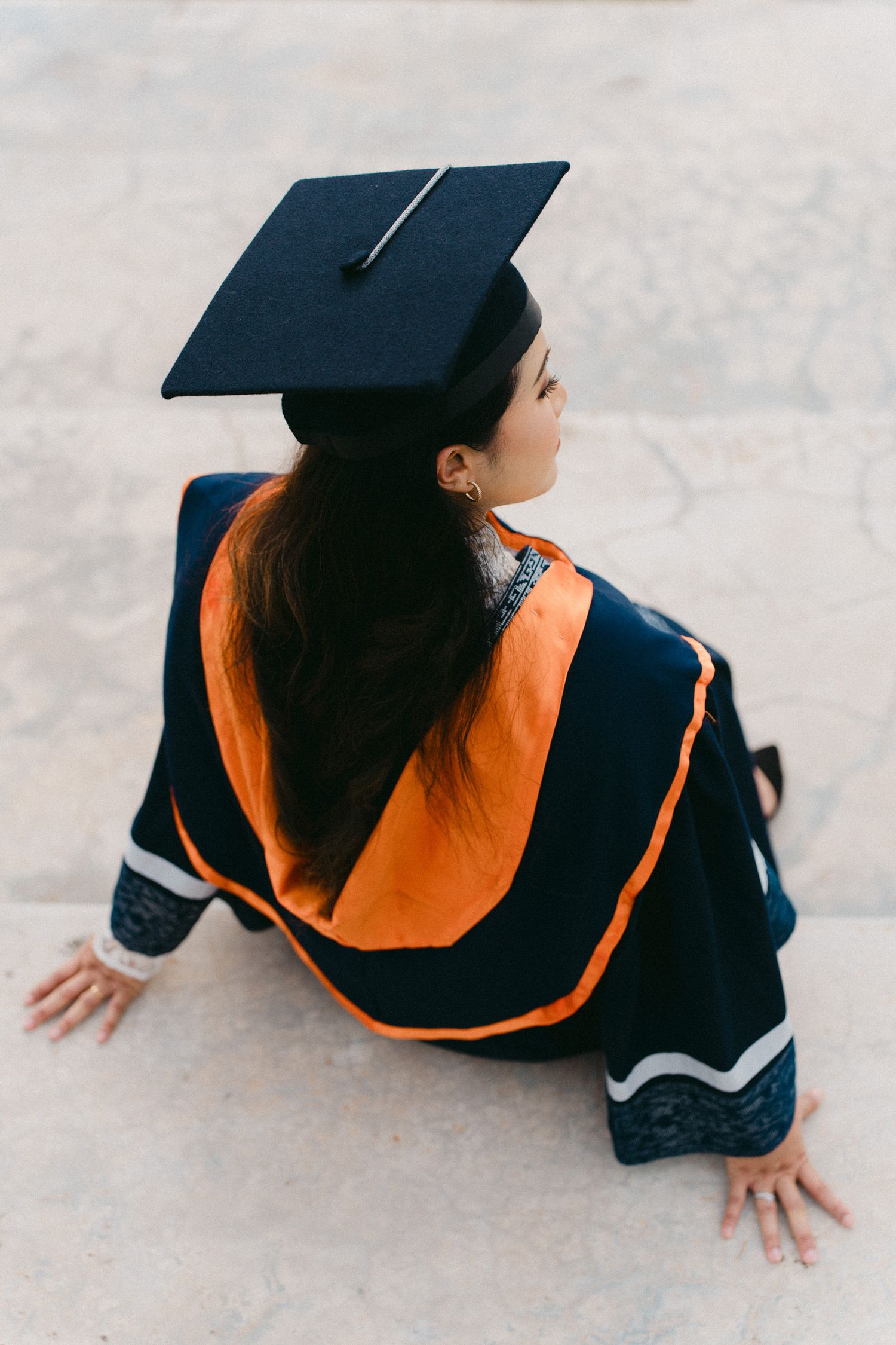 A graduate in black cap and gown with orange sash is photographed from above in a series of dynamic poses.