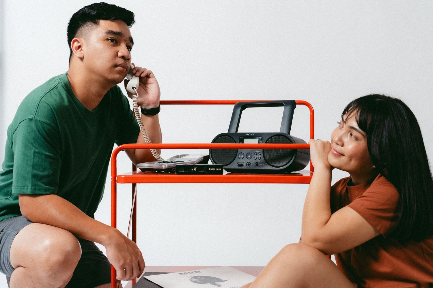 Young couple in casual attire sitting and posing thoughtfully in studio setting.