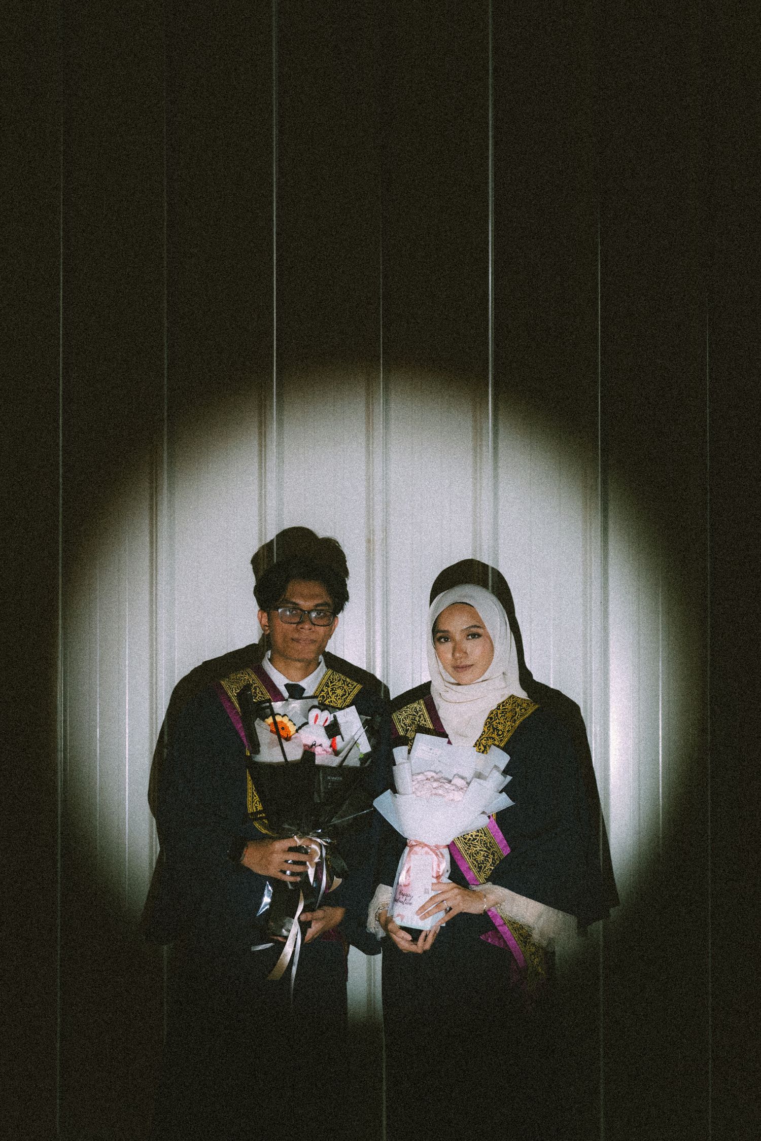 A couple poses with flowers against a spotlight-lit backdrop.