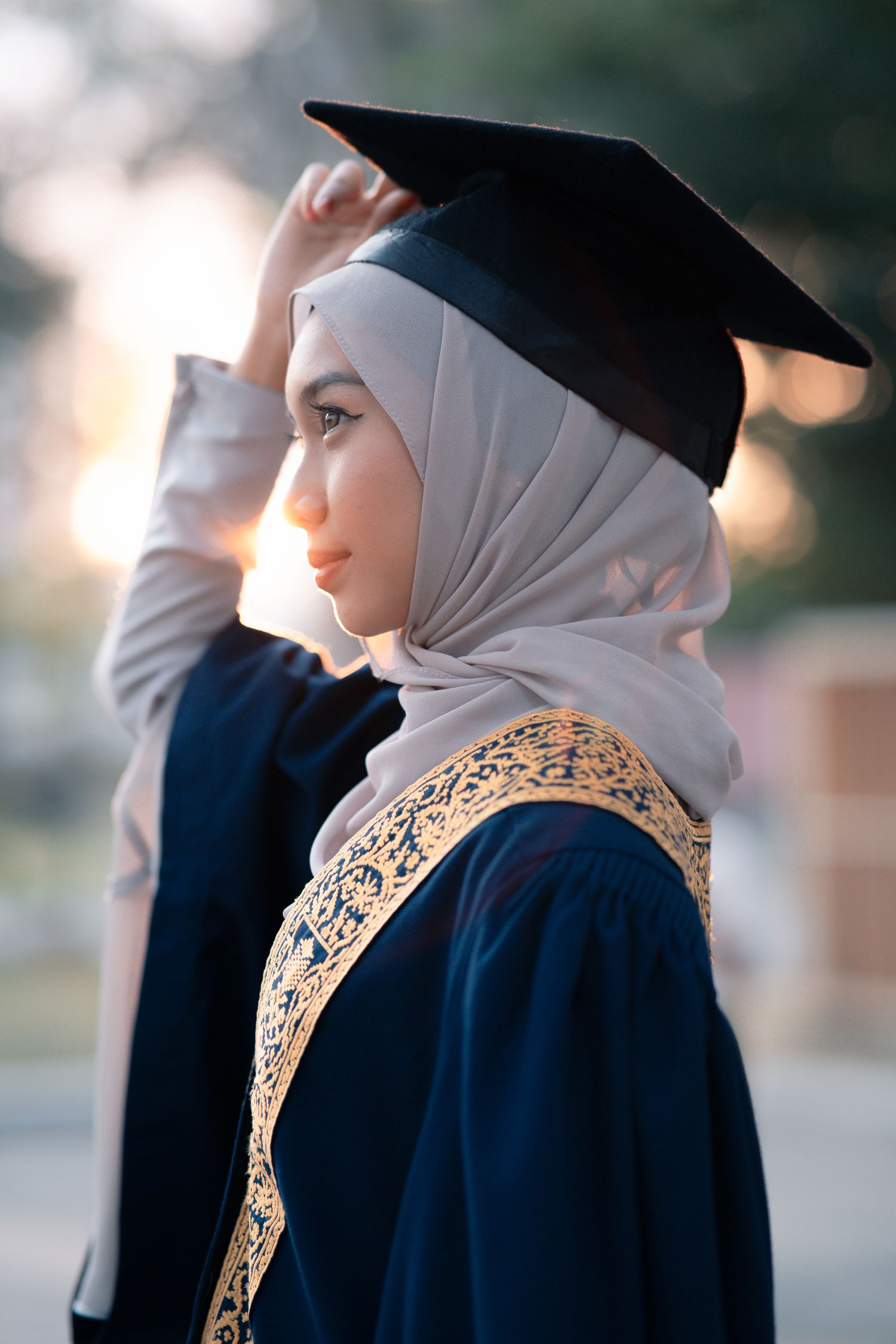 Profile view of graduate in ornate blue graduation gown and hijab.