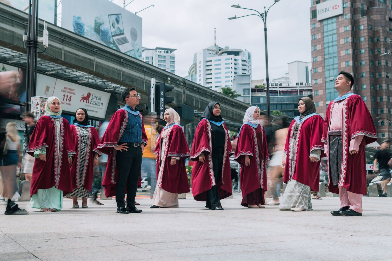 Graduates in red robes and traditional dress standing together on an urban street.