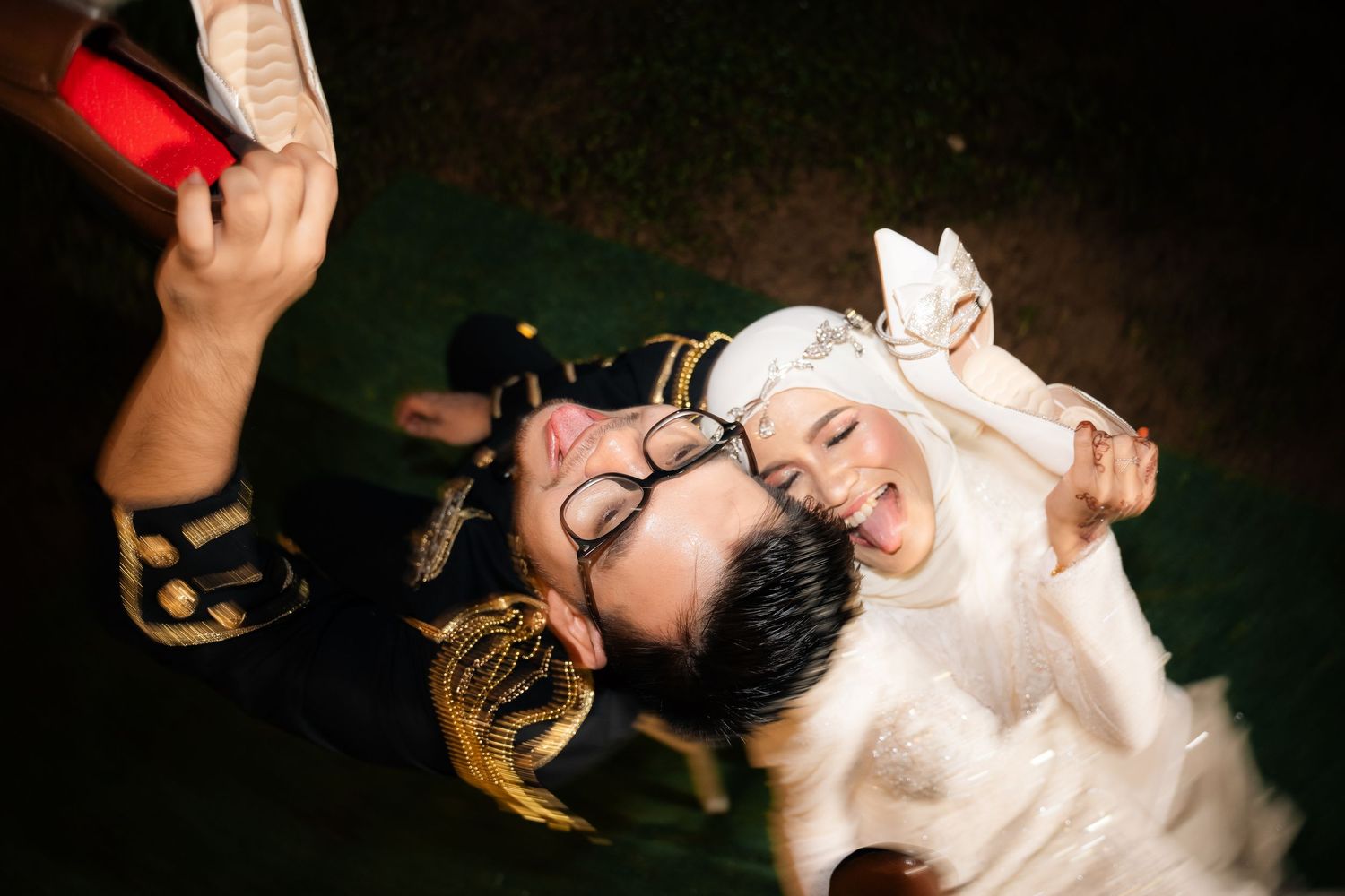 Birds-eye view of two people lying on dark floor laughing and taking overhead selfie photo together.
