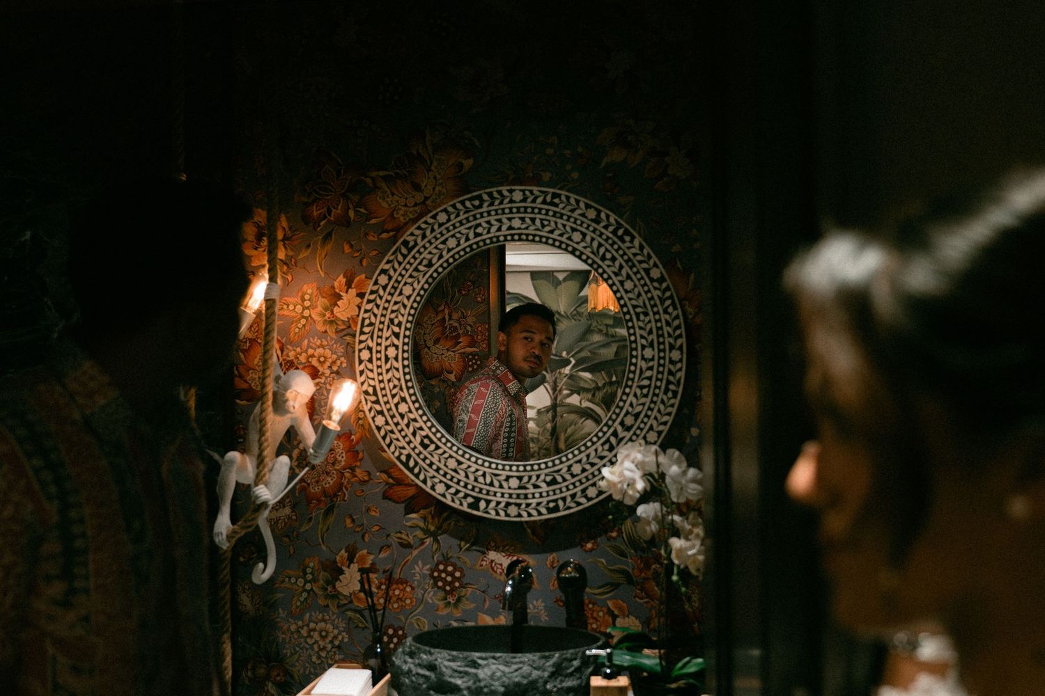 A decorative mirror with a rhinestone frame hangs on a dark rustic wall in moody lighting.