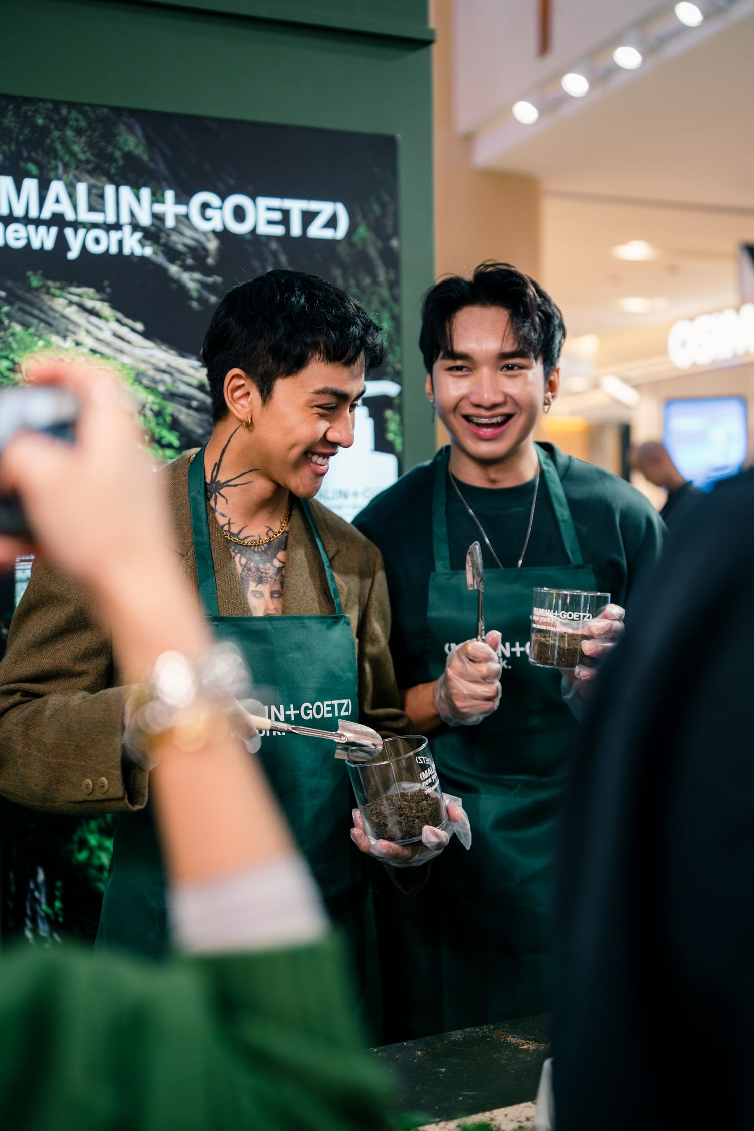 Staff members in green aprons serve customers at Malin+Goetz product demonstration.