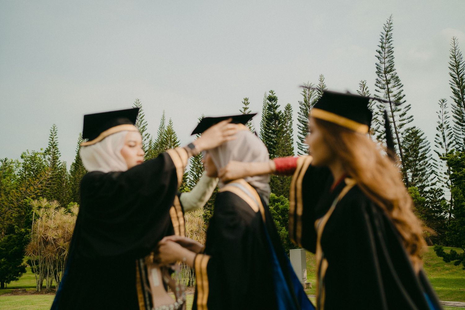 Graduates in black caps and gowns share a joyful moment adjusting their graduation caps.