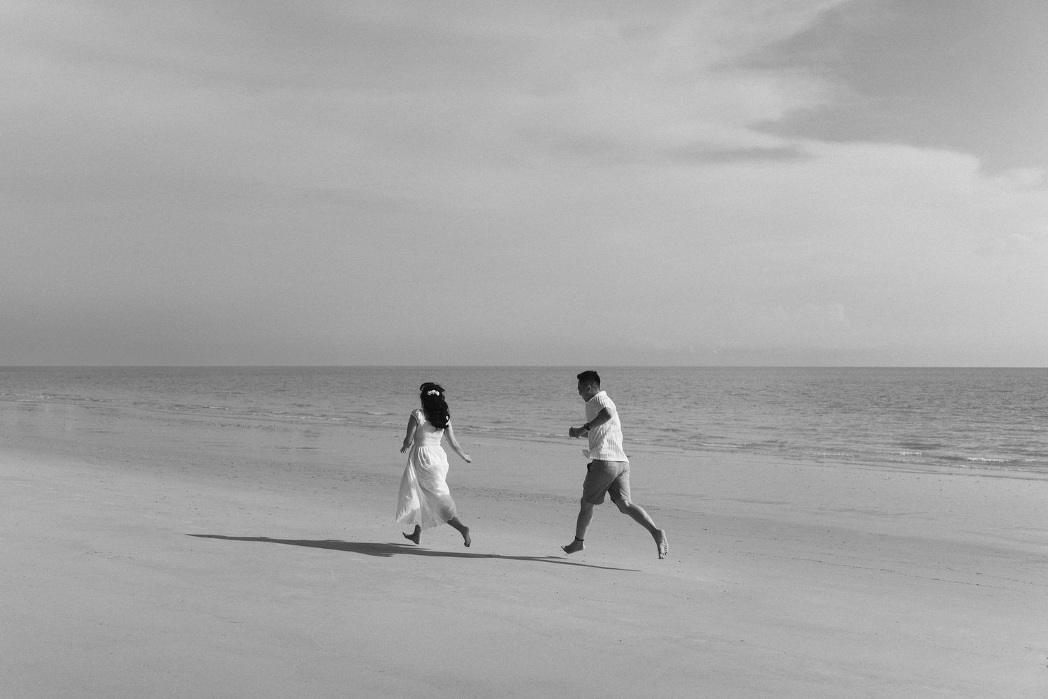 Two people running along an empty beach shore in black and white photography.