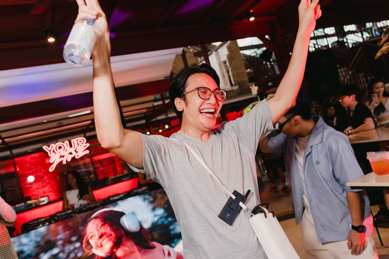 Crowd of people dancing and celebrating at a lively indoor party with colorful lighting and festive atmosphere.