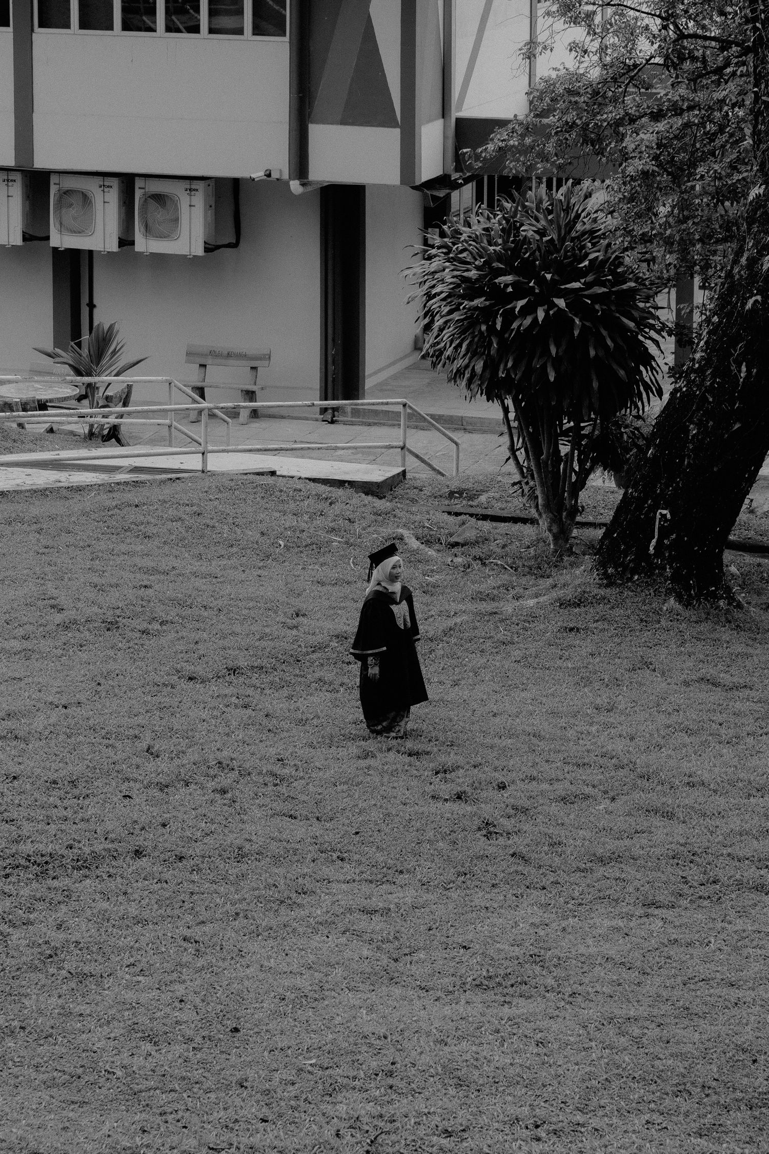 A sequence of black and white photos showing a person walking down a grassy slope near a building.