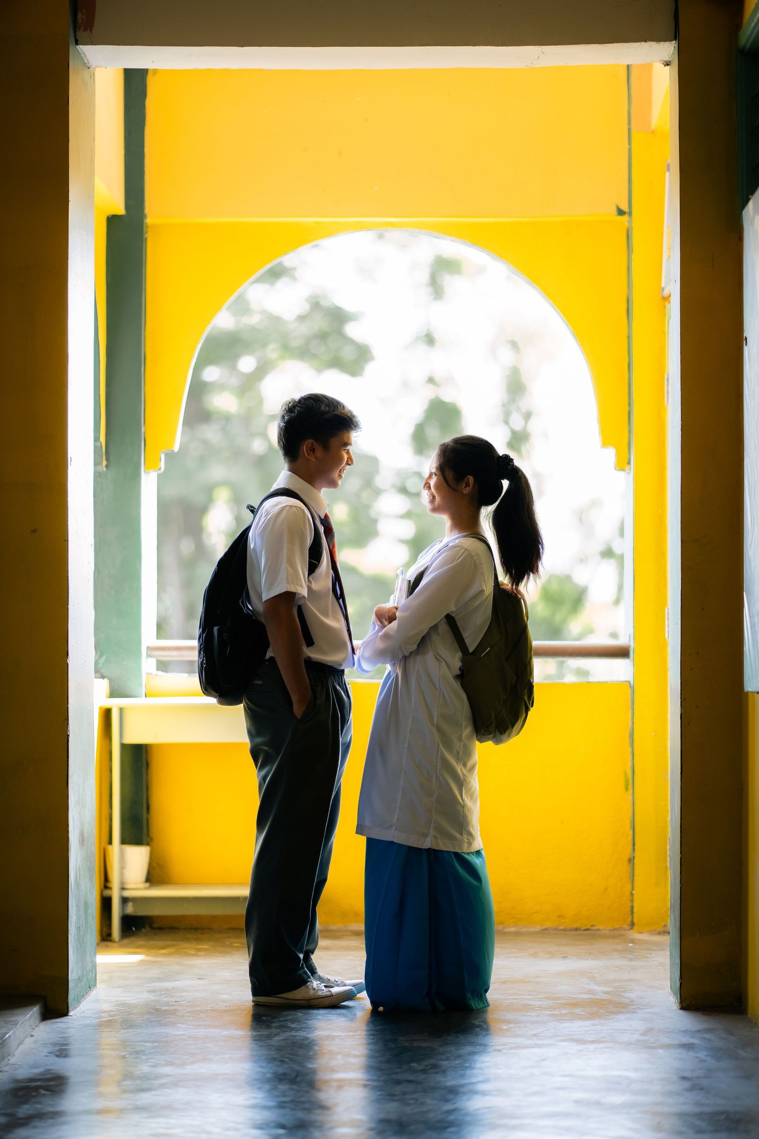 Two students having a conversation under a yellow archway in a school corridor.