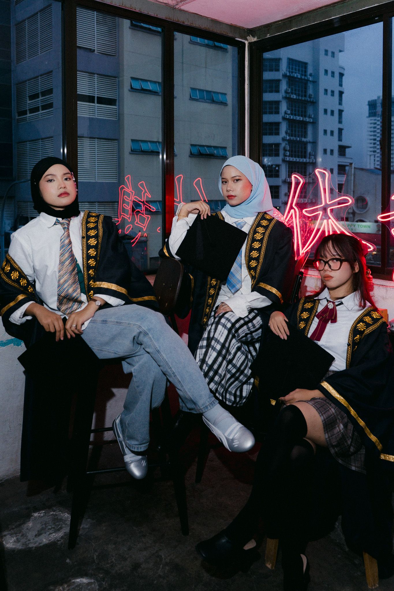 Three young women in school uniforms and hijabs pose near neon signs in an urban setting.