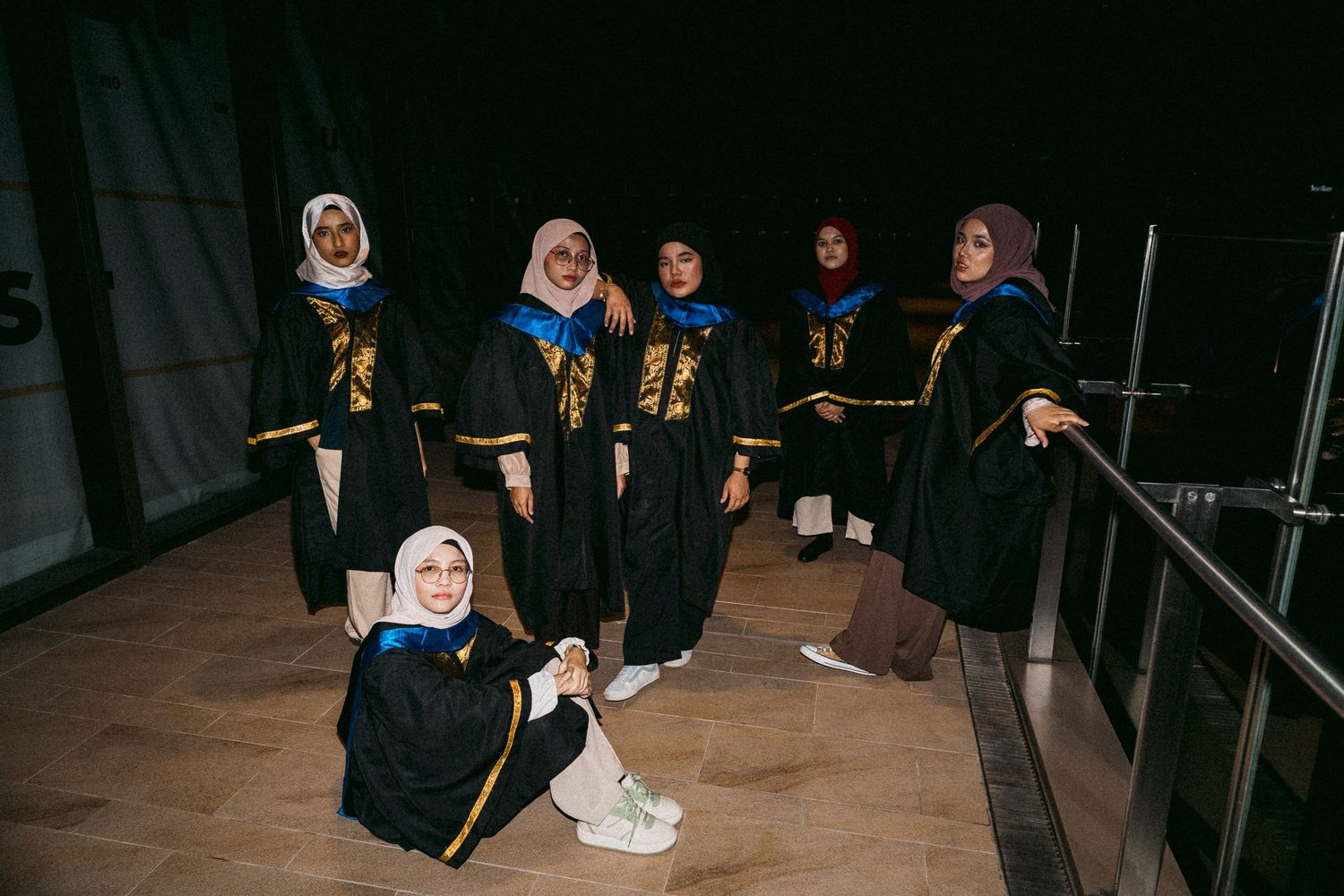 Graduates in black and gold robes pose casually in a dark setting.