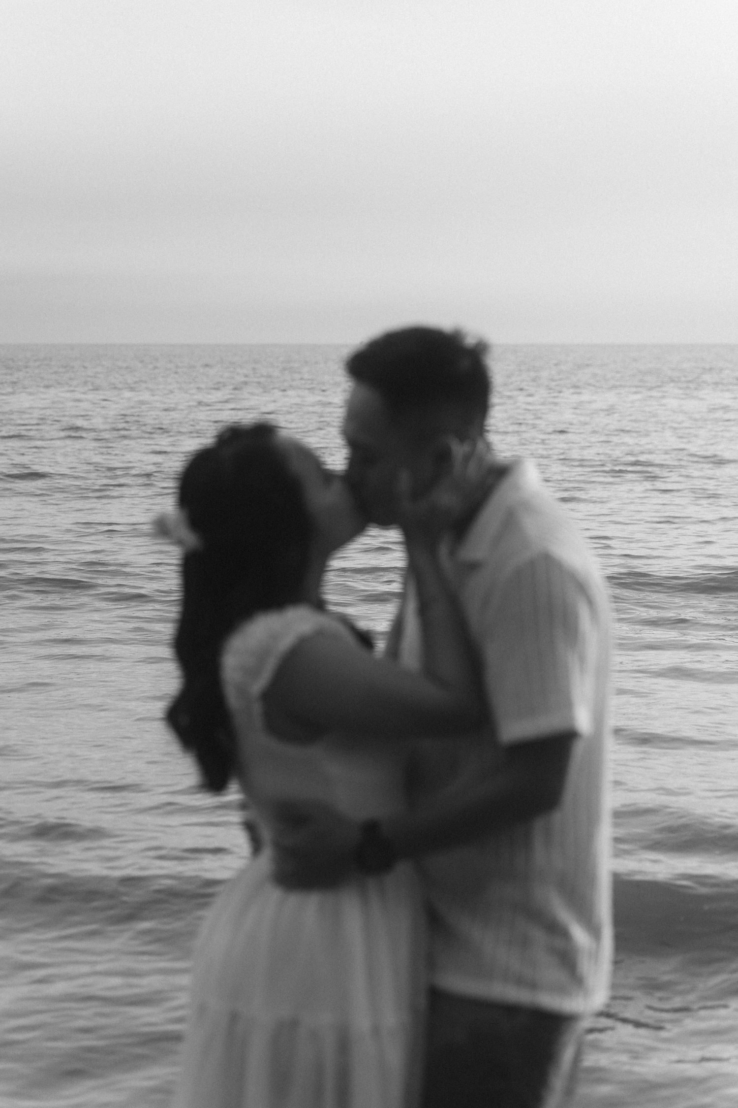 A romantic couple shares a tender kiss on a misty beach at sunset.