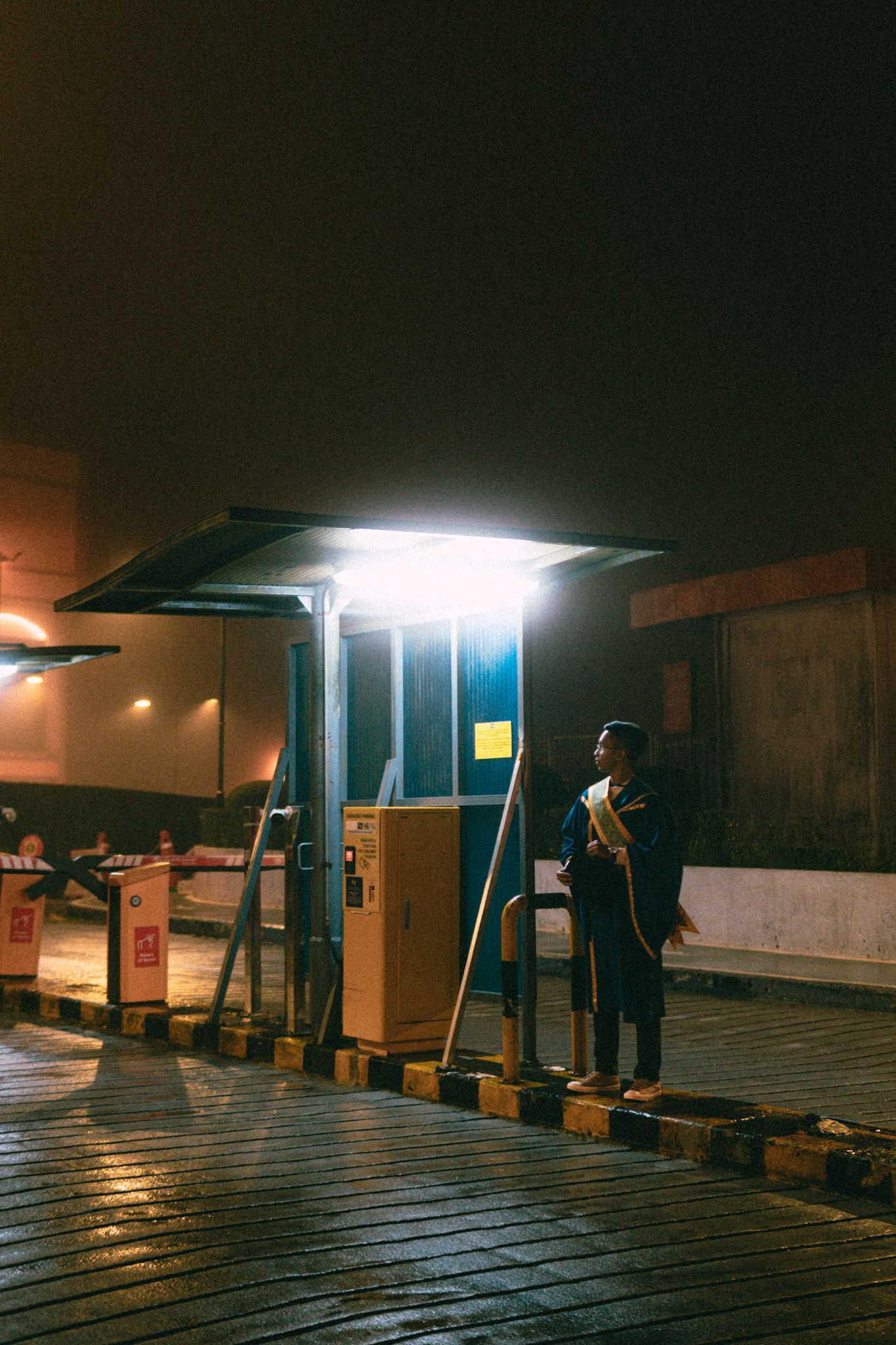 Person standing under illuminated shelter at night with ambient lighting.