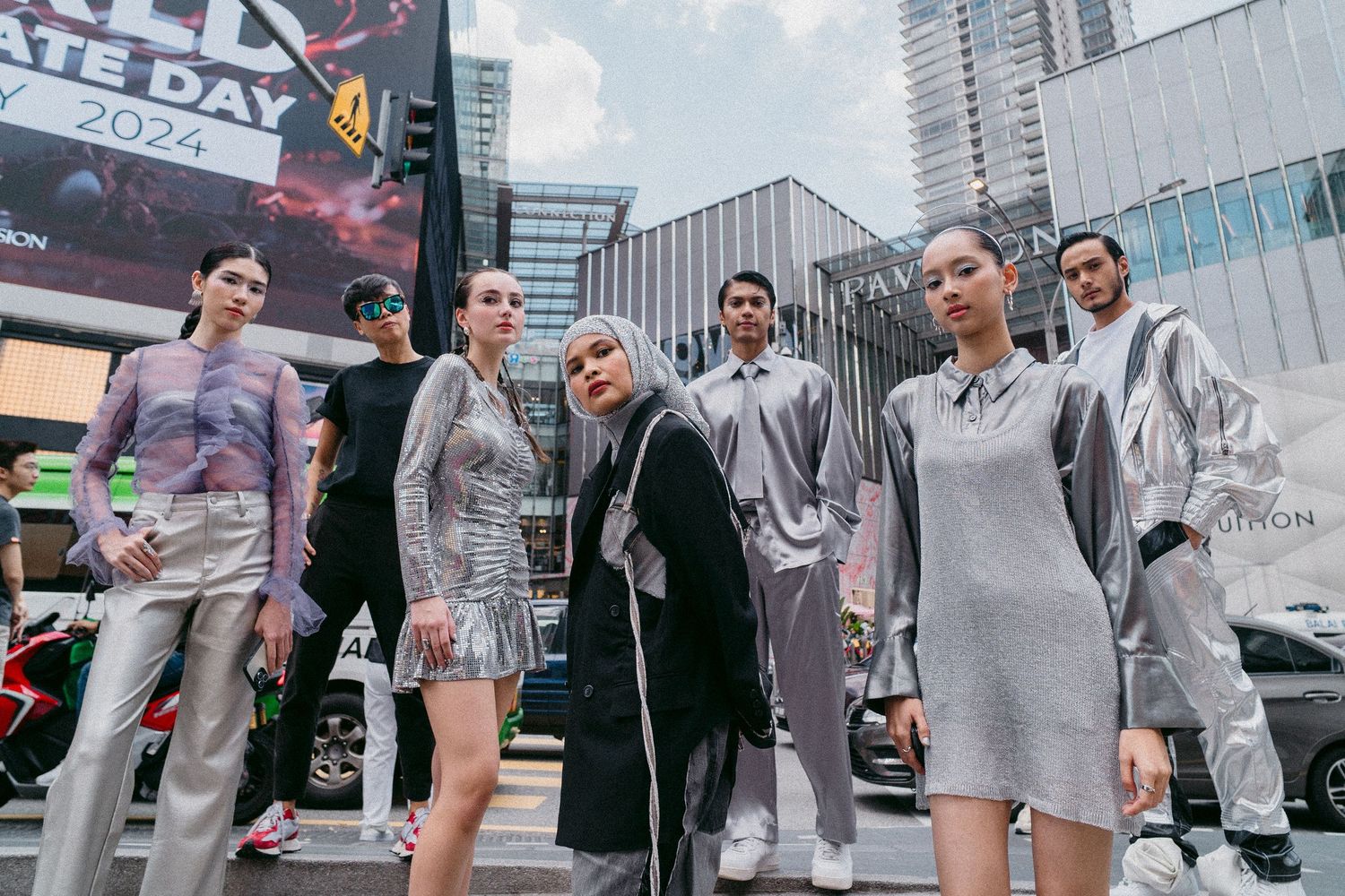 Group wearing coordinated silver and gray outfits posing in an urban setting with skyscrapers.