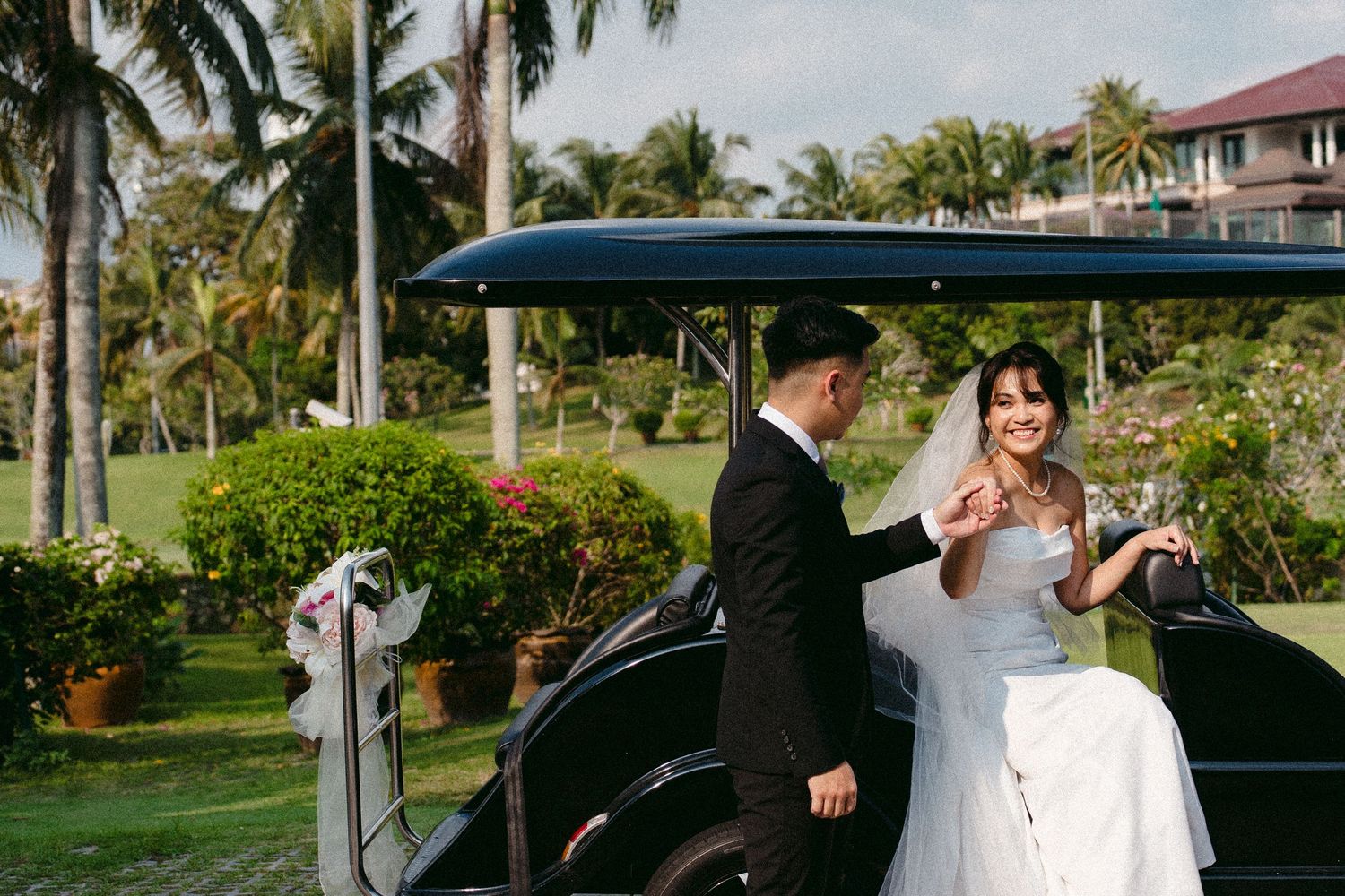 Newlywed couple posing by a golf cart on a tropical palm-lined course with decorative bows.