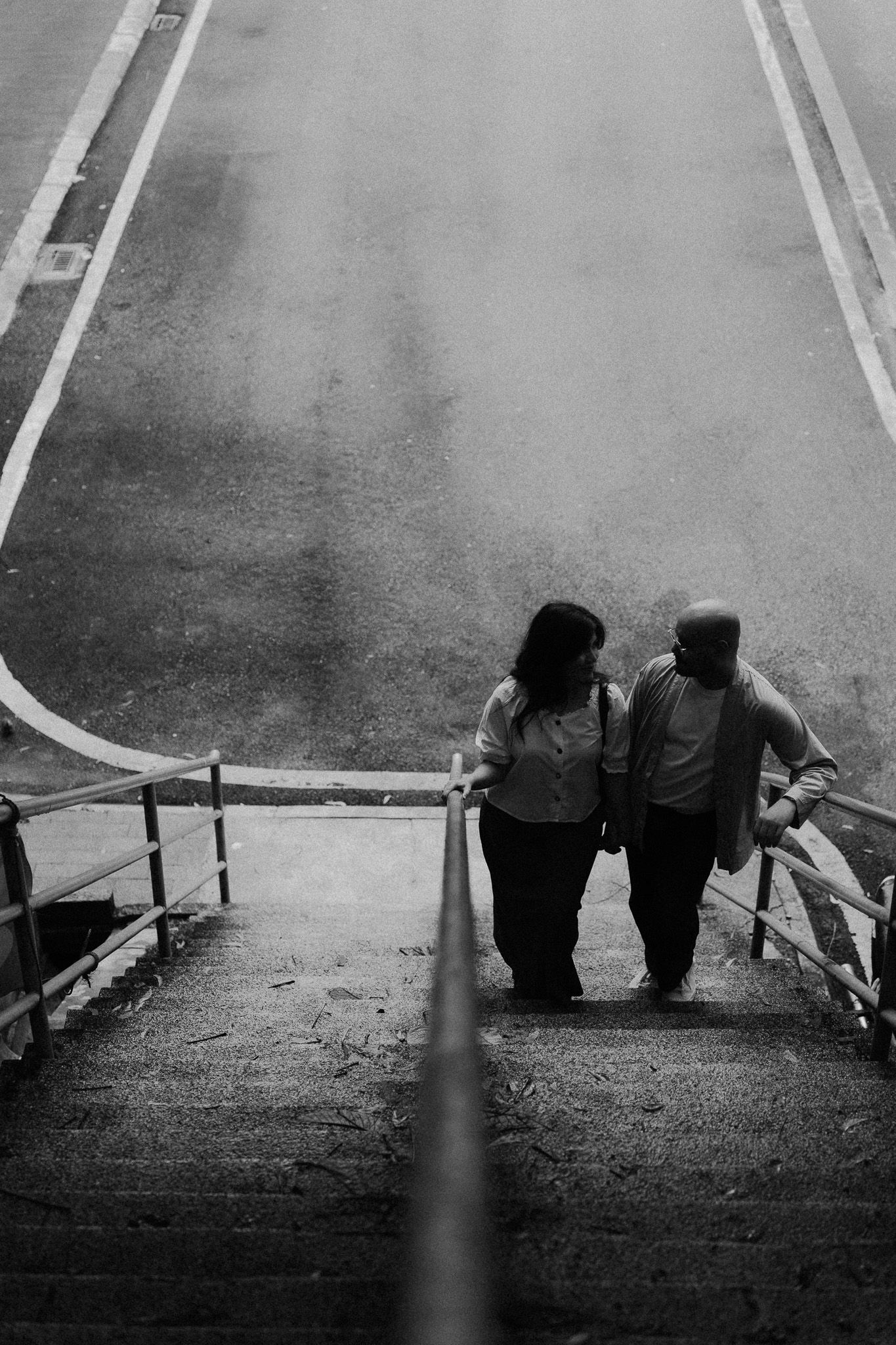 A couple walks down outdoor stairs together in a black and white photo, viewed from above.