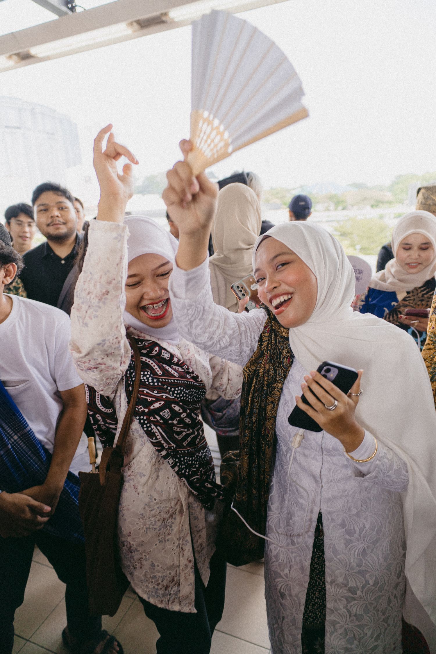 Celebrating attendees in white hijabs and traditional dress holding up decorative fans.