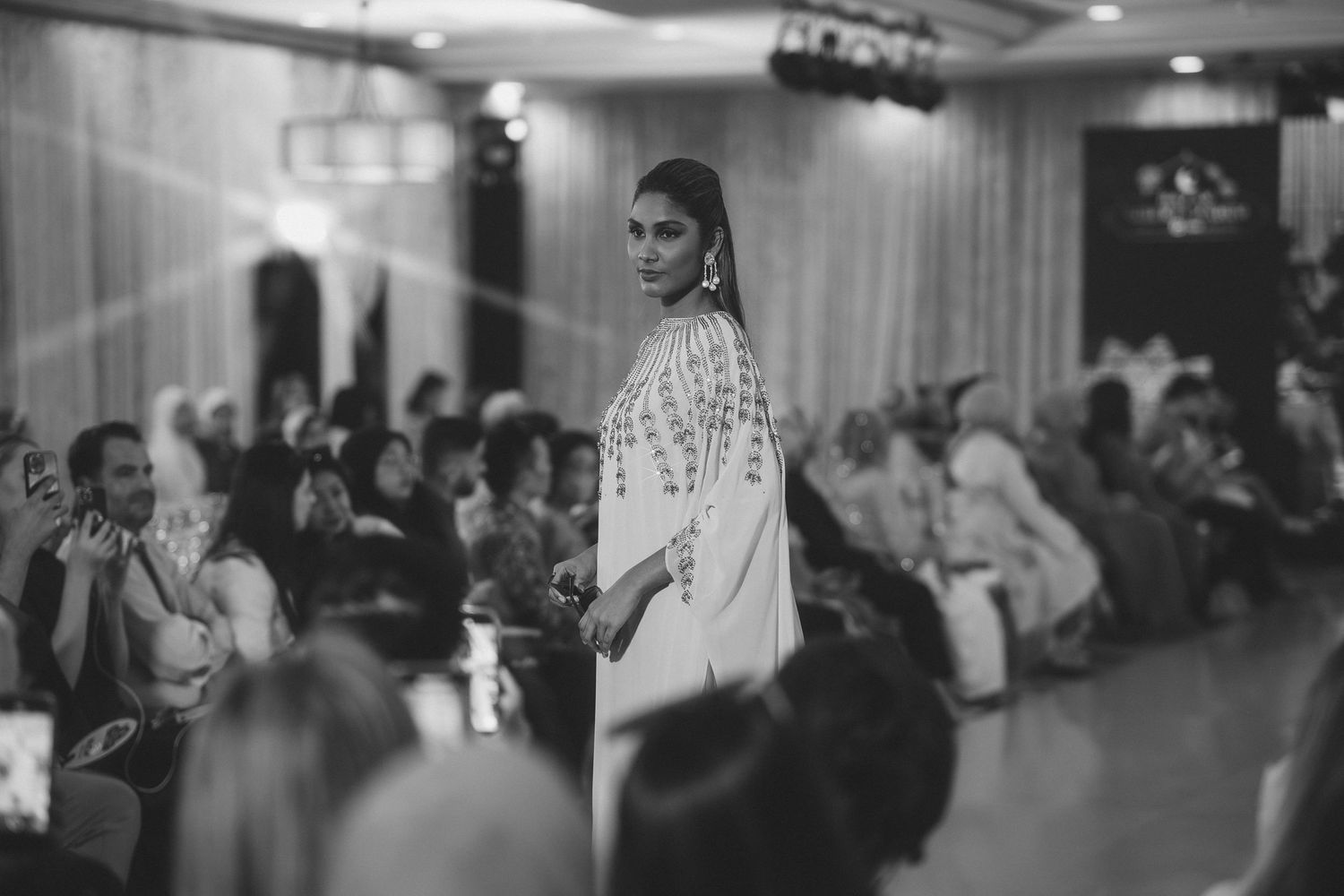 Black and white photo of fashion show featuring elegant evening wear on runway.