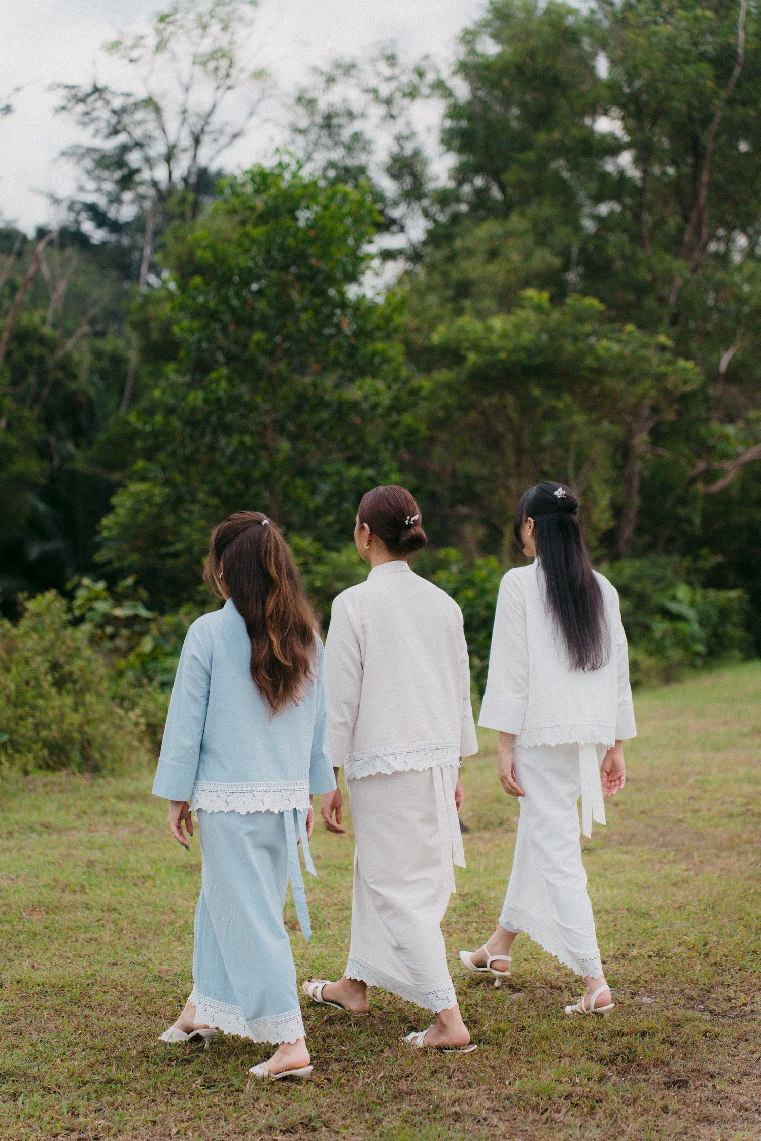 Three models in coordinated pastel outfits walking through green outdoor setting.