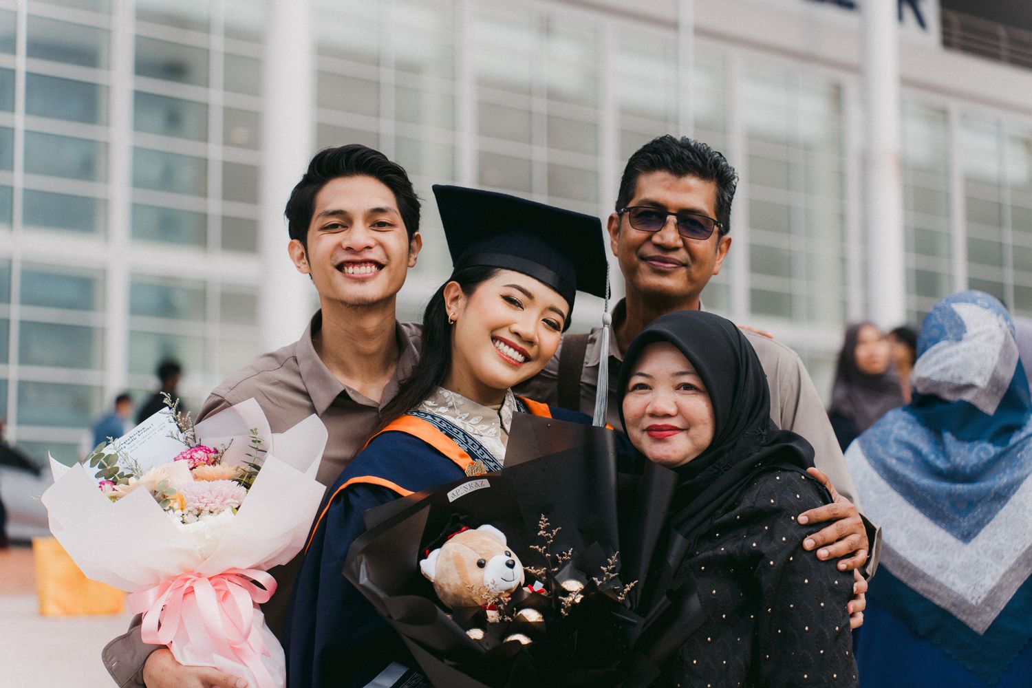 A group of friends celebrating graduation day with flowers and smiles outdoors.