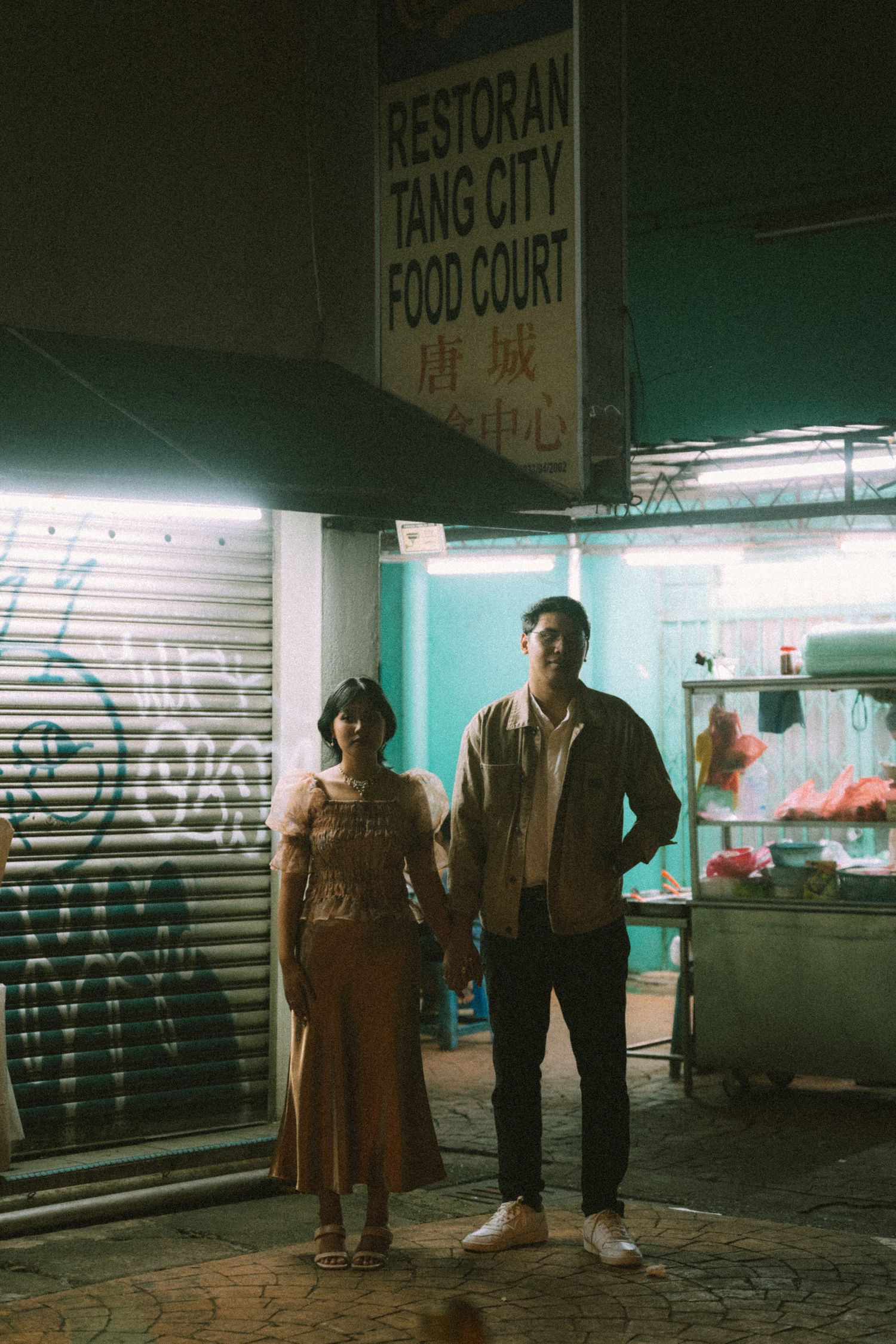 Couple standing outside Tang City Food Court at night with urban backdrop.