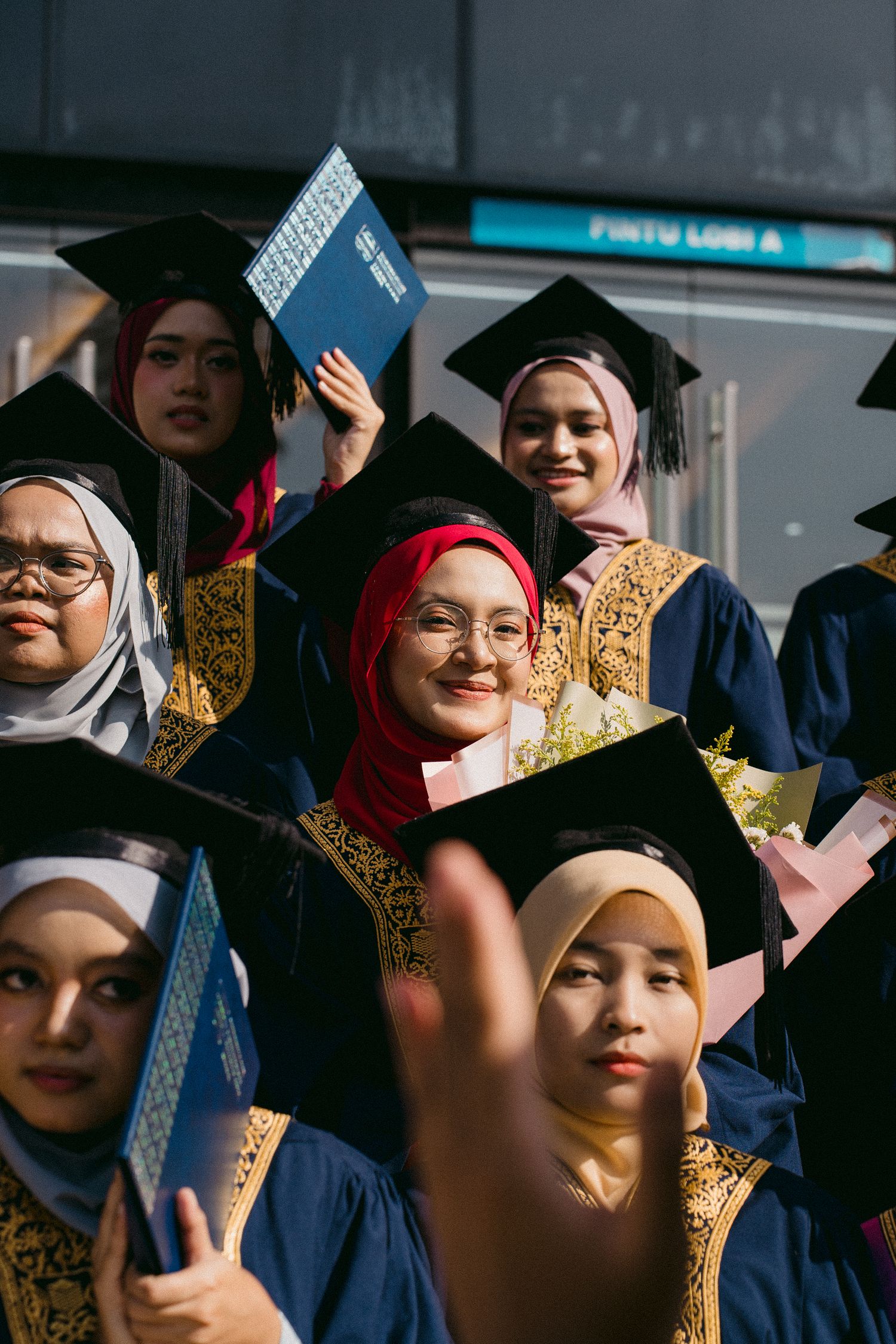 Graduates in navy blue robes and ornate stoles celebrating while holding their diplomas.