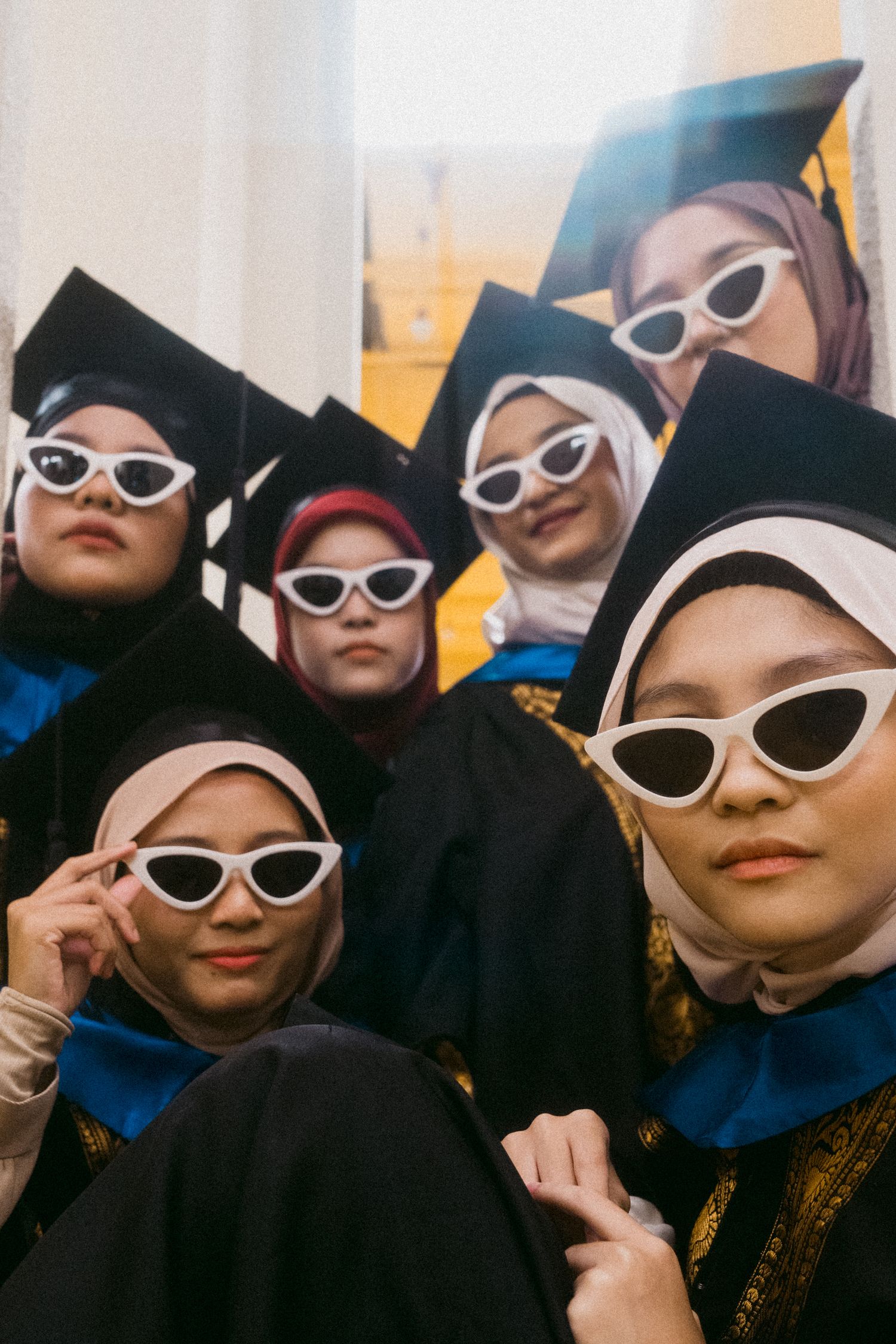 Graduates wearing white cat-eye sunglasses strike a pose in their graduation regalia.