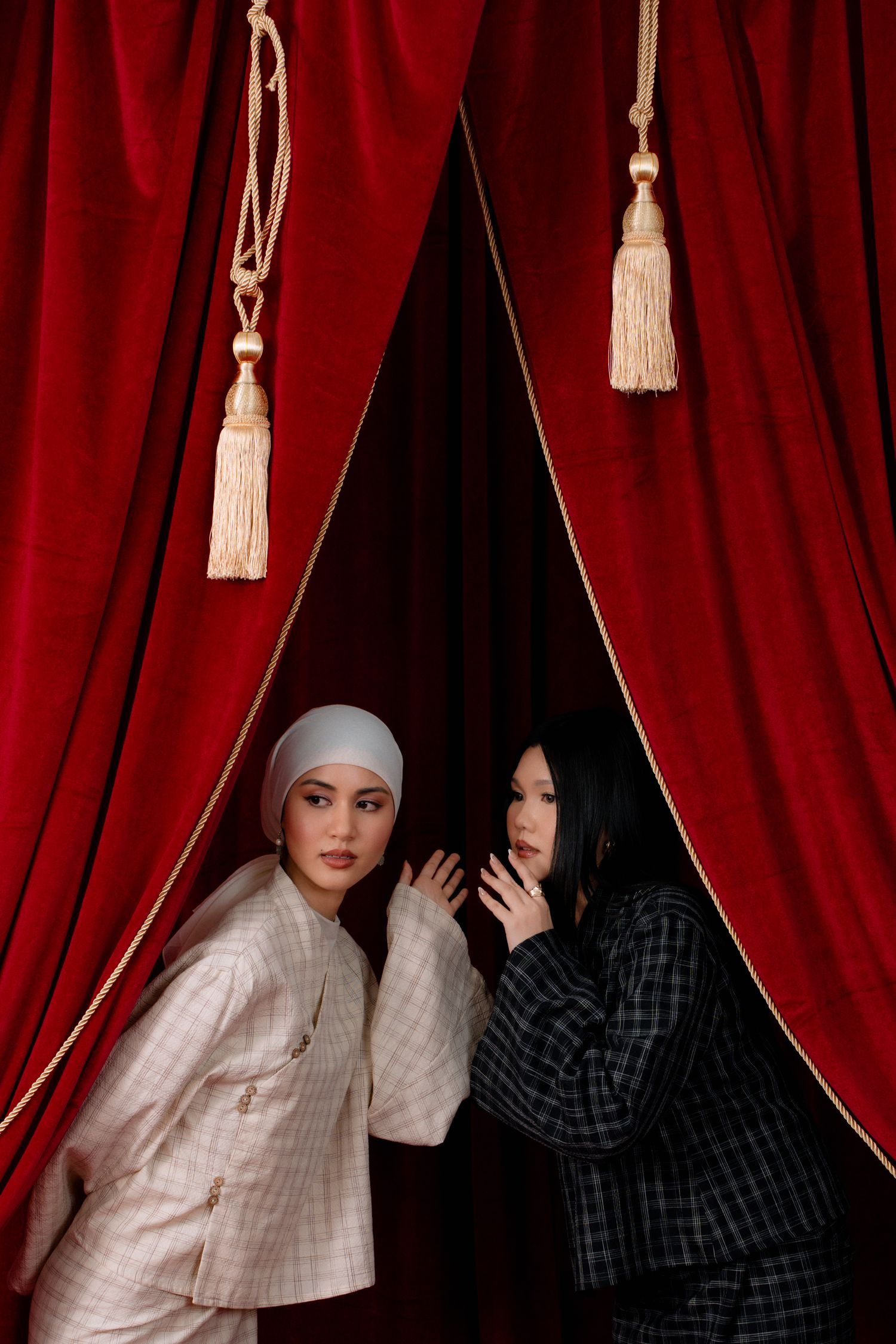 Two figures in contrasting white and black outfits pose dramatically against red velvet theater curtains.