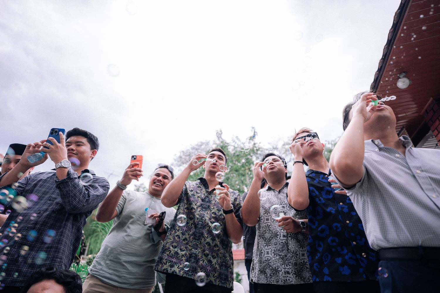 Group of people blowing and photographing colorful soap bubbles outdoors at a festive gathering.