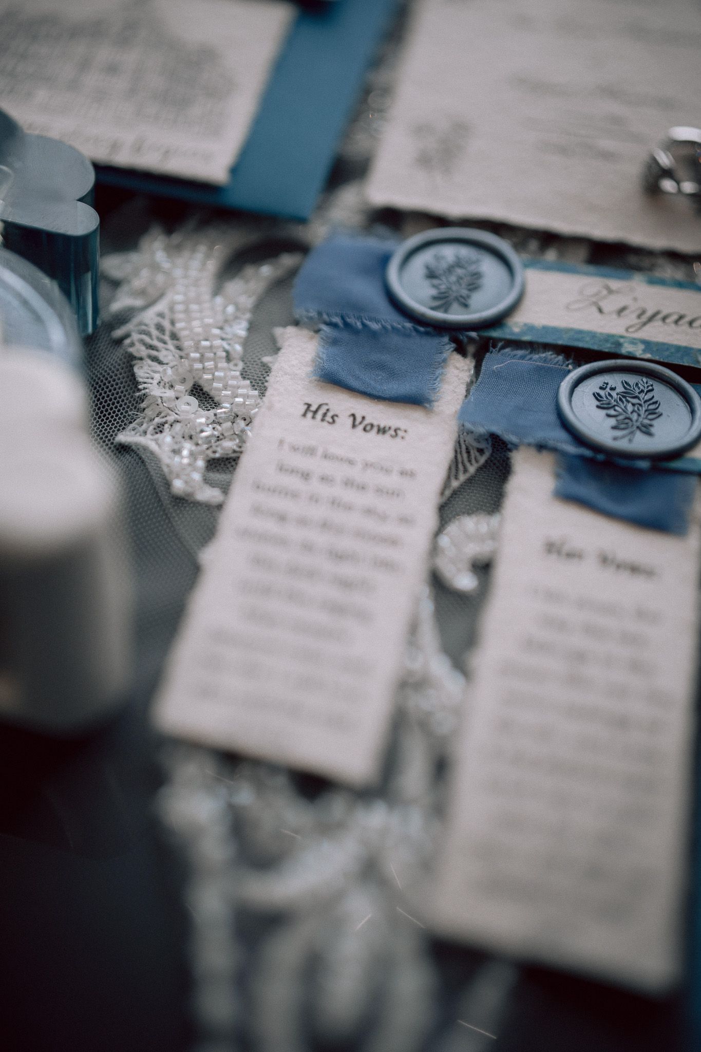 Elegant wedding vow cards with blue wax seals, pearl details, and ribbon on a decorative flat lay display.