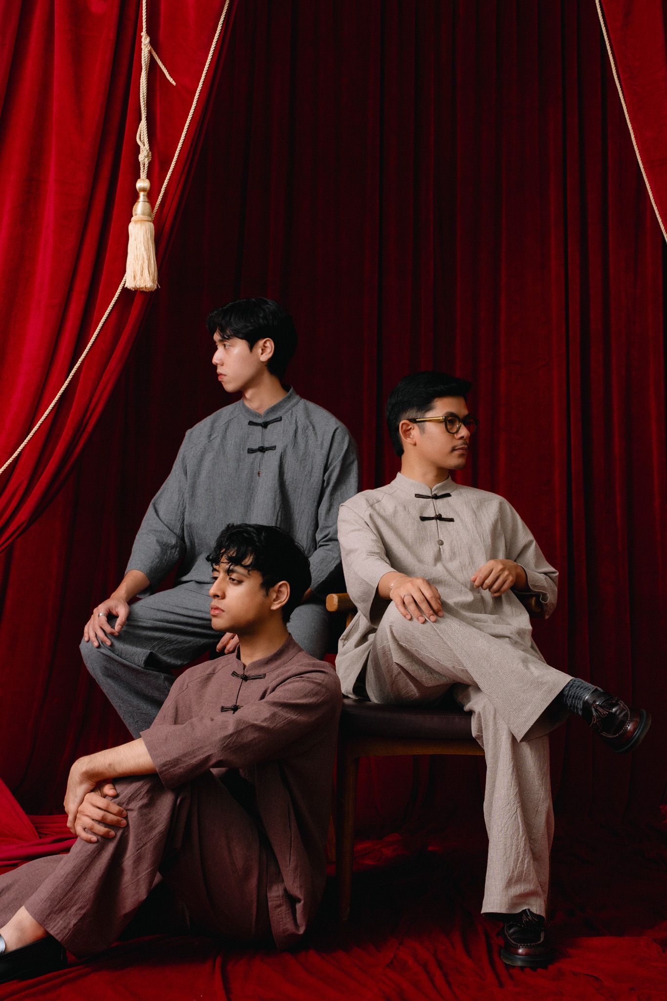 Three men in traditional Chinese linen outfits posing against red velvet curtains.