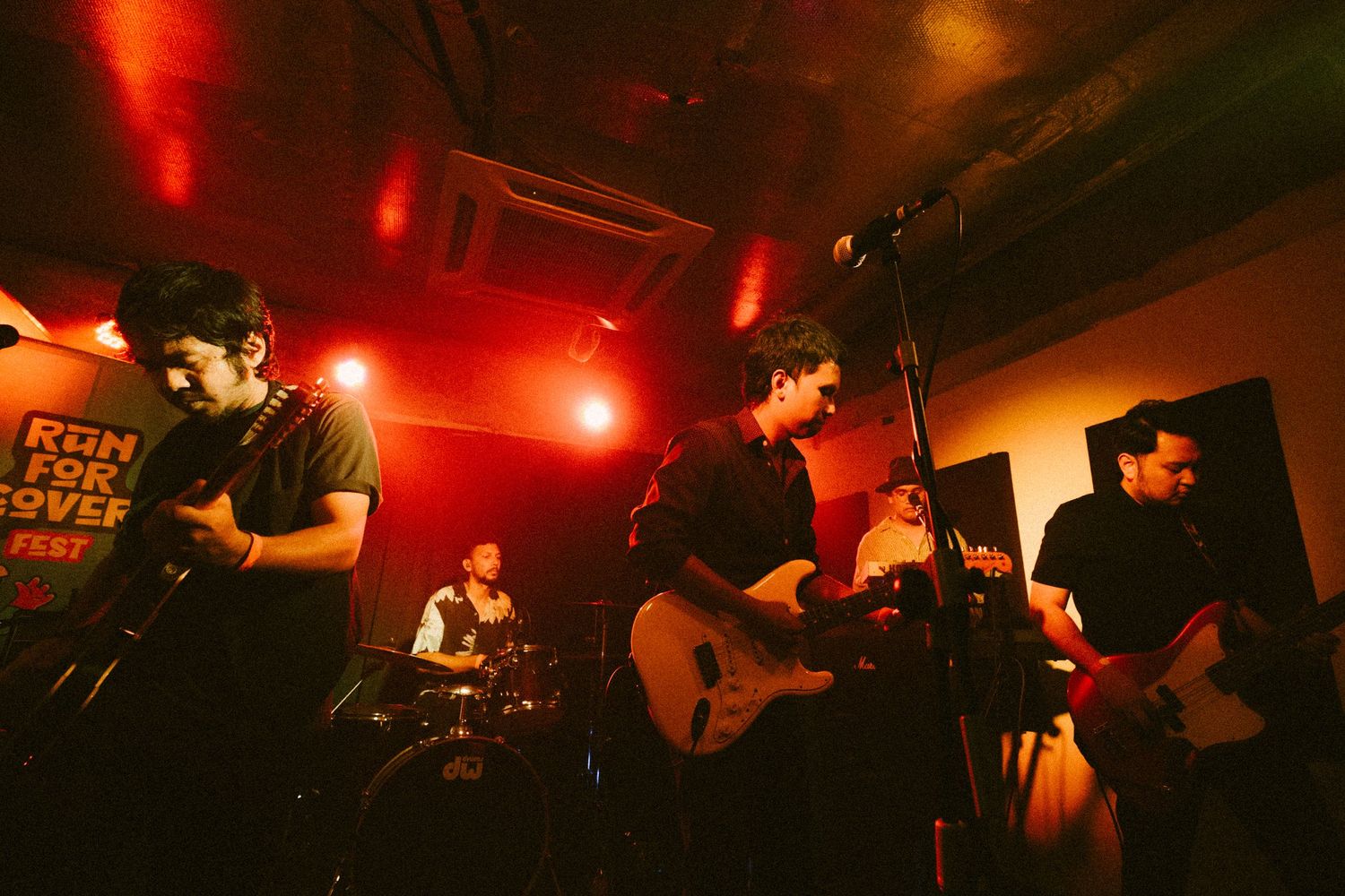 Band performing on stage in a dimly lit venue with red lighting and musical instruments.