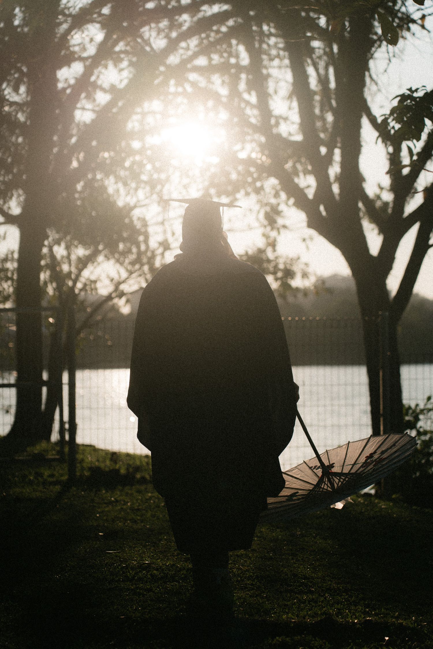 A silhouetted figure stands against a misty sunset backdrop with trees and a lake creating a moody atmospheric scene.