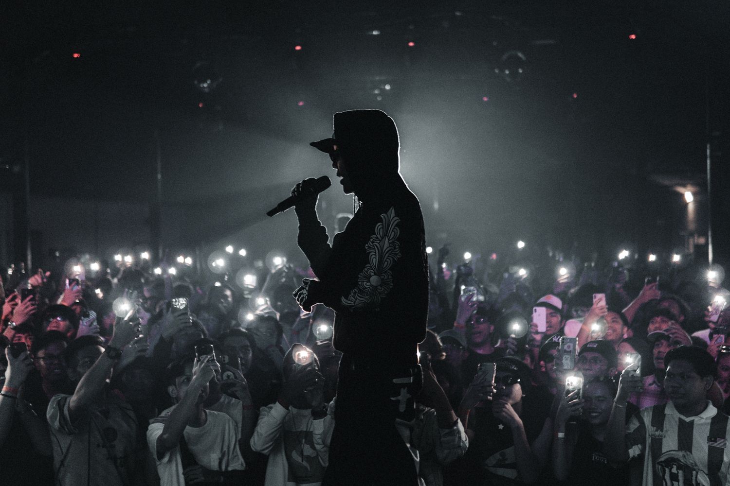 Performer silhouetted on stage with crowd holding up glowing phone lights.