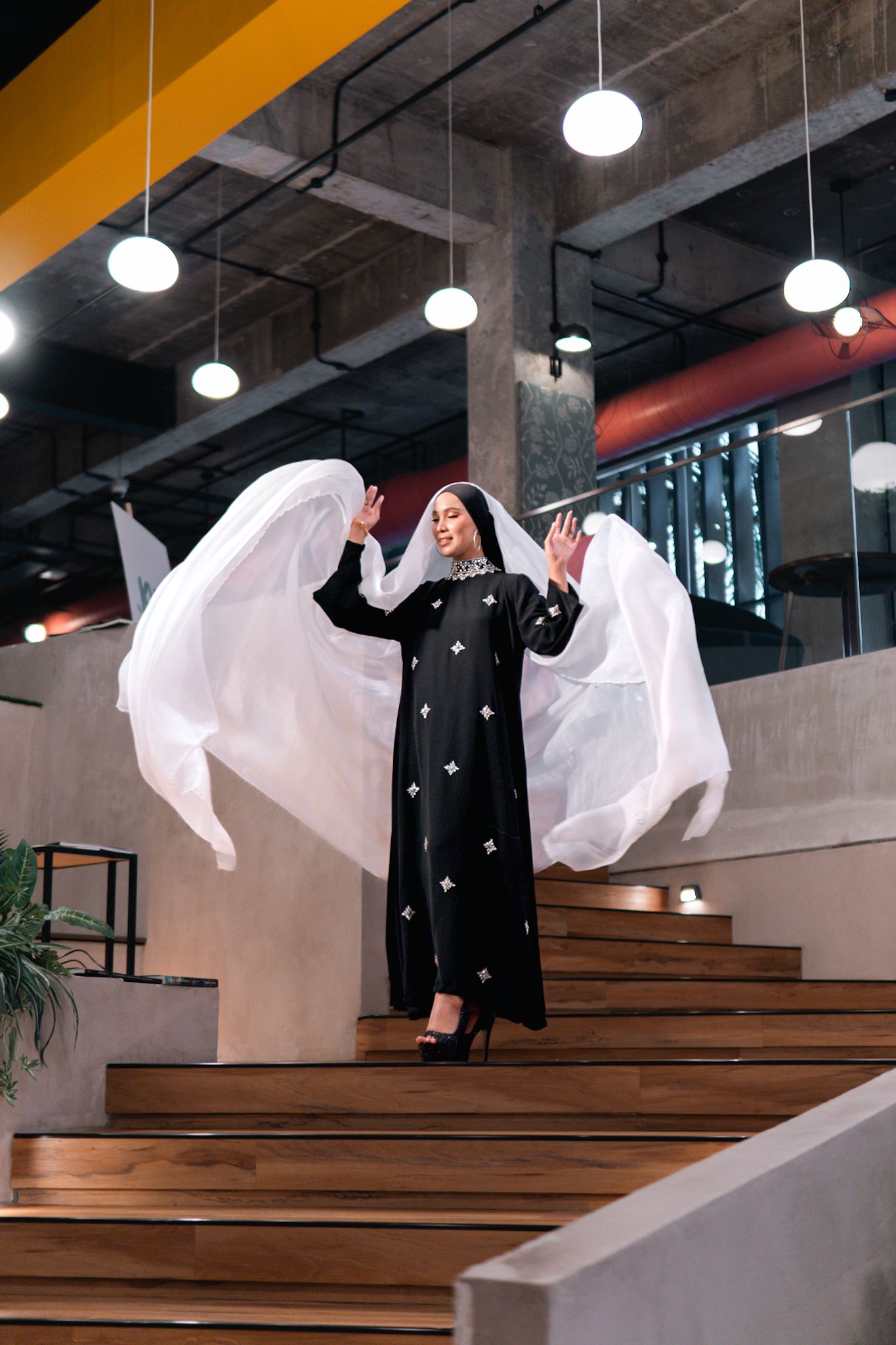 Long black dress with flowing white fabric creating dramatic movement on wooden stairs.