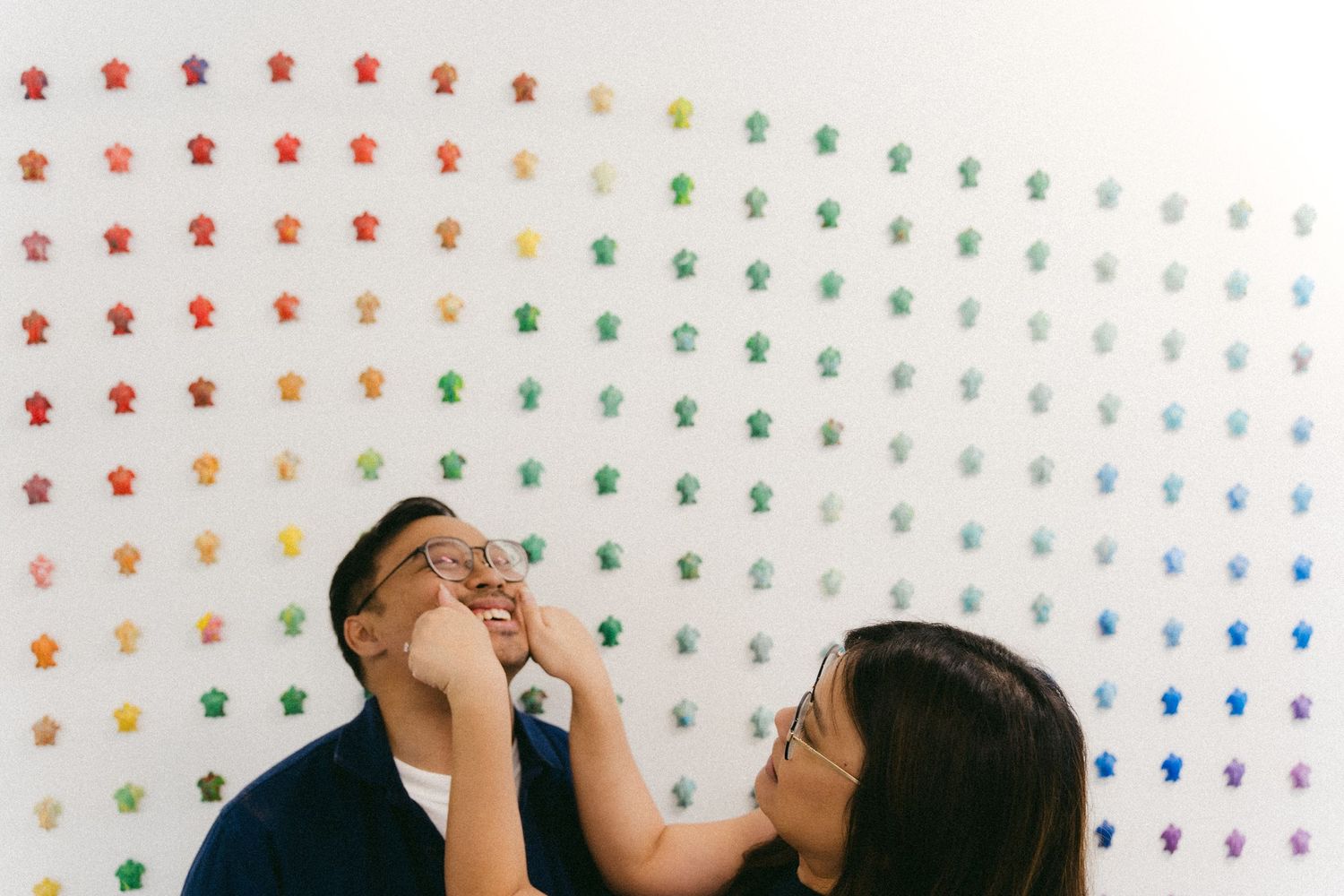 A couple shares a playful moment in front of a colorful polka dot wall.