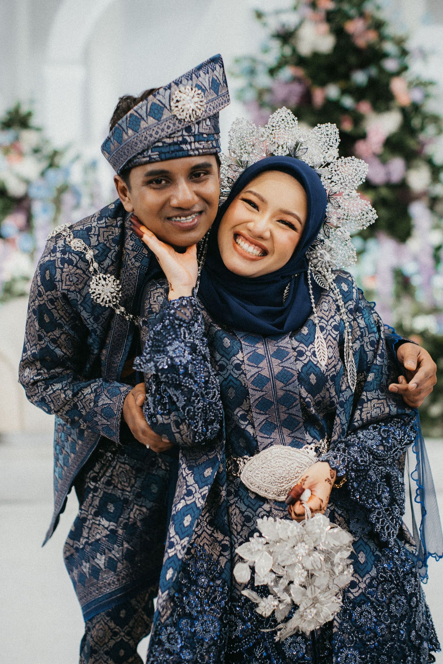 Traditional Malaysian wedding couple in matching navy blue outfits sharing joyful moments during their photoshoot.