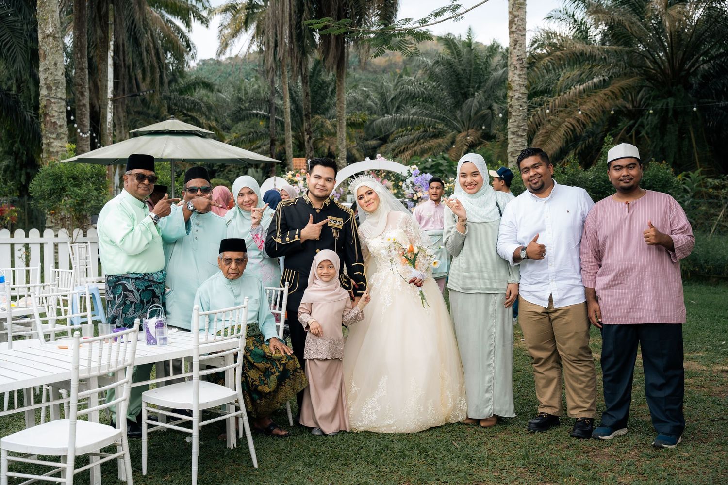 Guests gathered under palm trees for an outdoor wedding ceremony with white chairs and decor in a tropical setting.