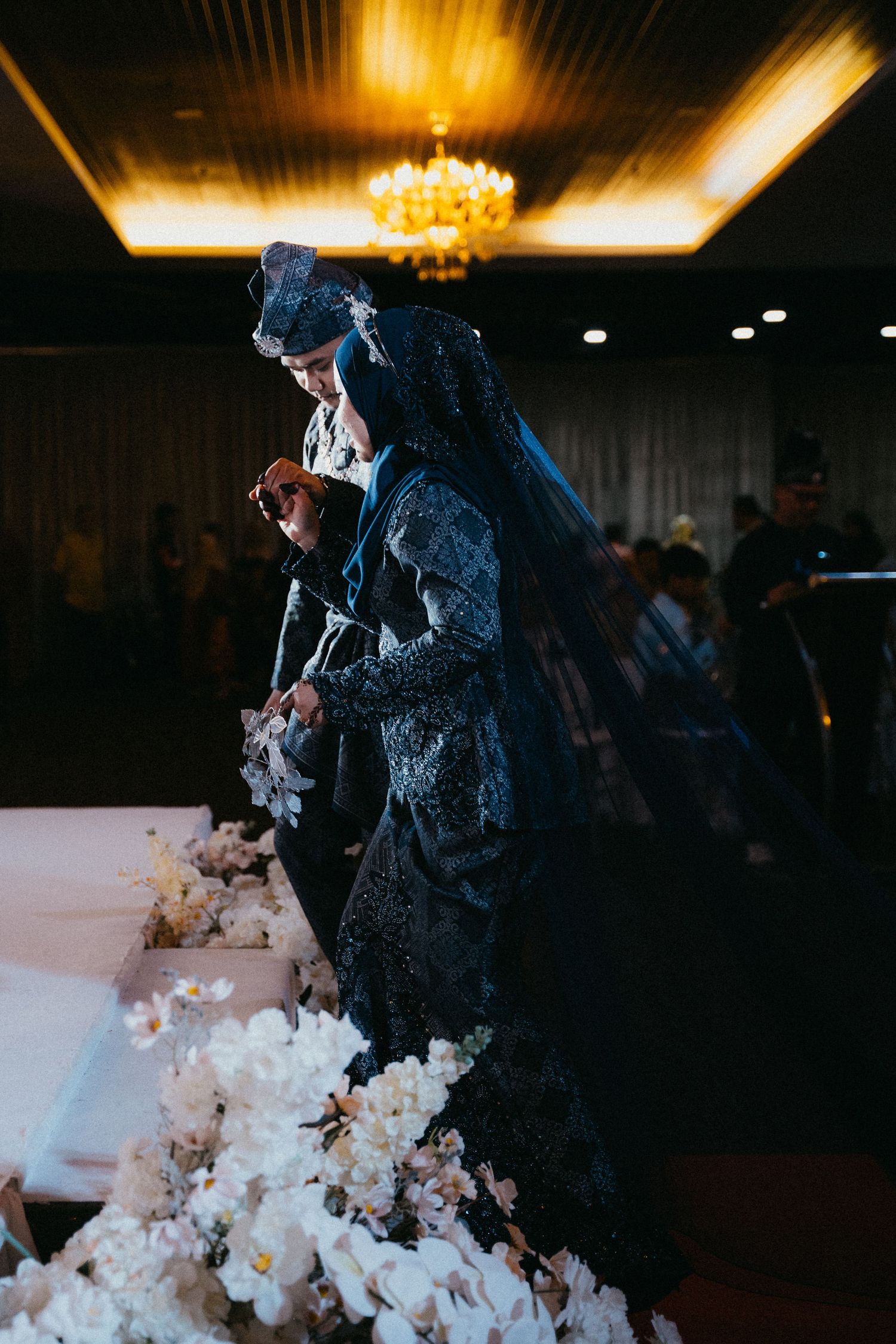 A wedding cake being cut with a gold chandelier overhead during an evening reception.