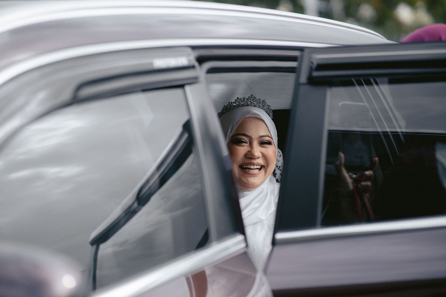 A bride in an elegant white wedding gown and veil sits gracefully in a luxury car.
