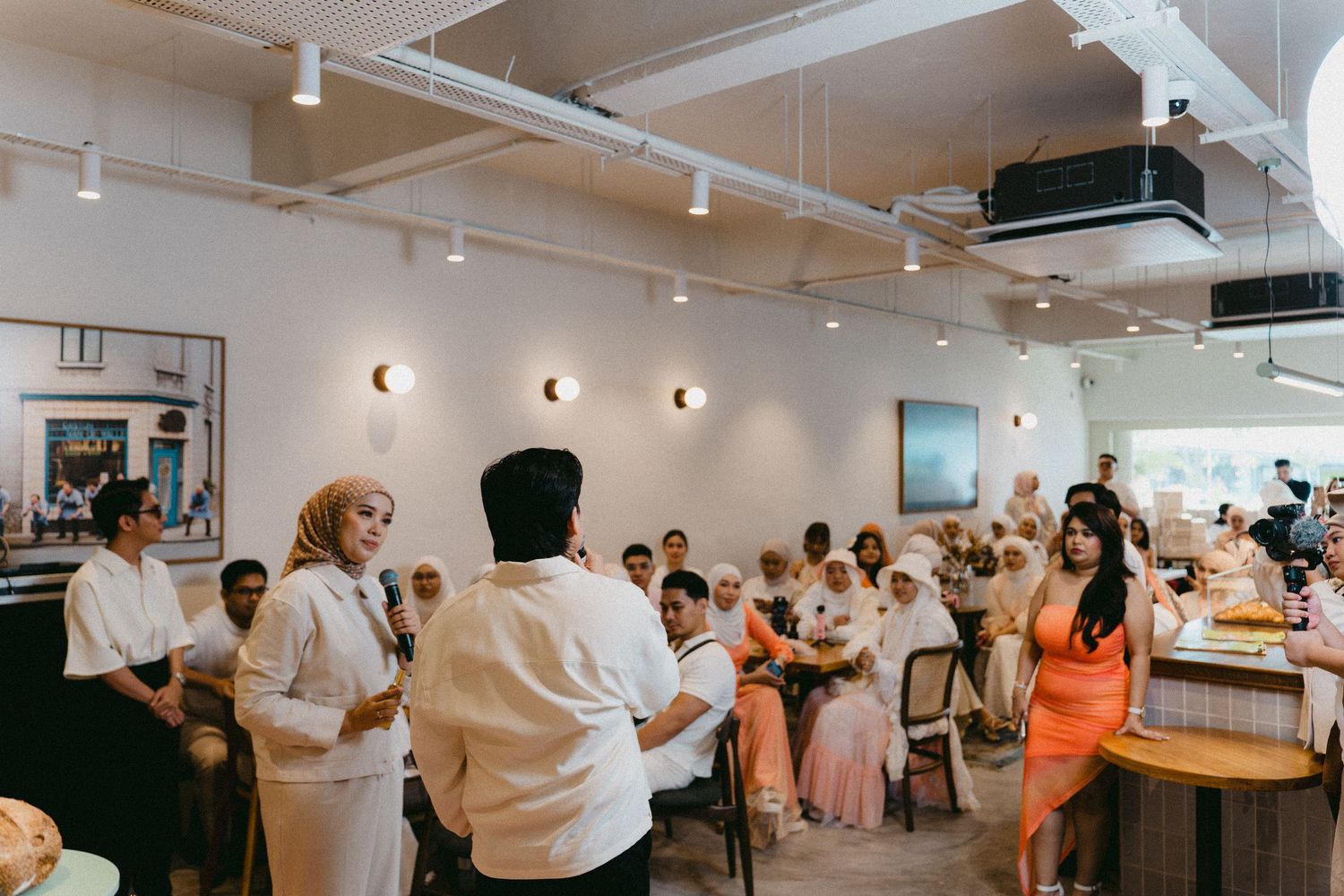 Crowd gathering in a modern white cafe interior with track lighting.