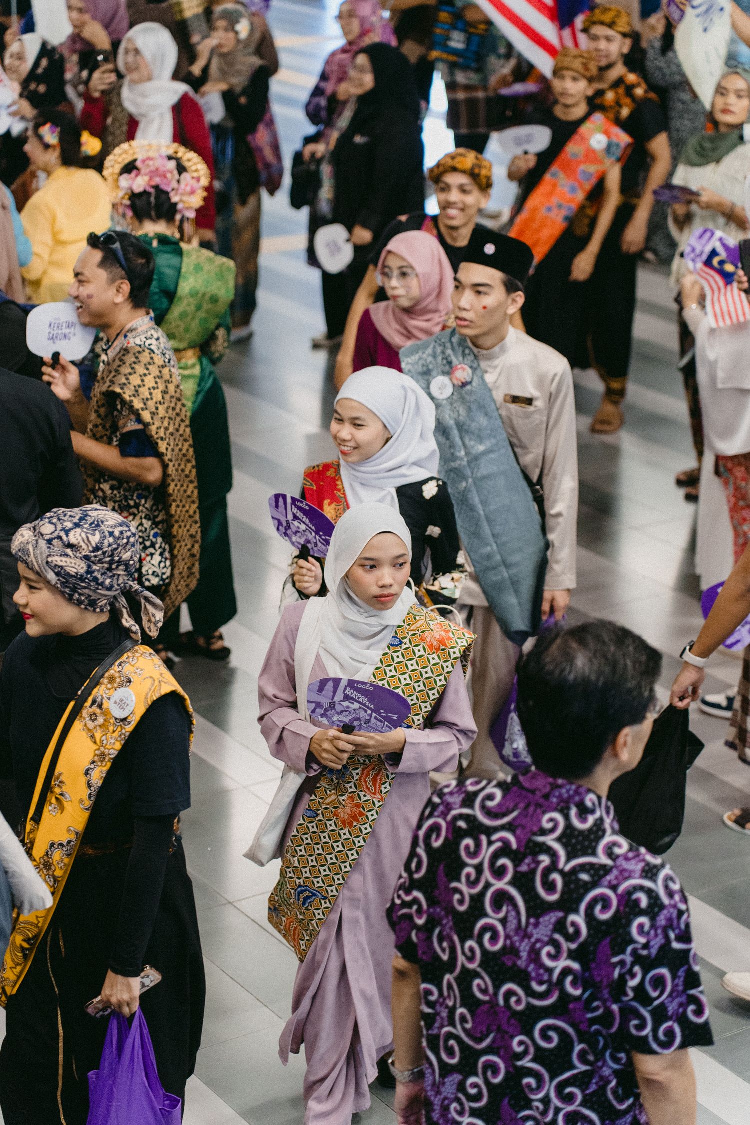 Diverse crowd in traditional and modern attire gathering at a cultural celebration with colorful traditional dress and hijabs.