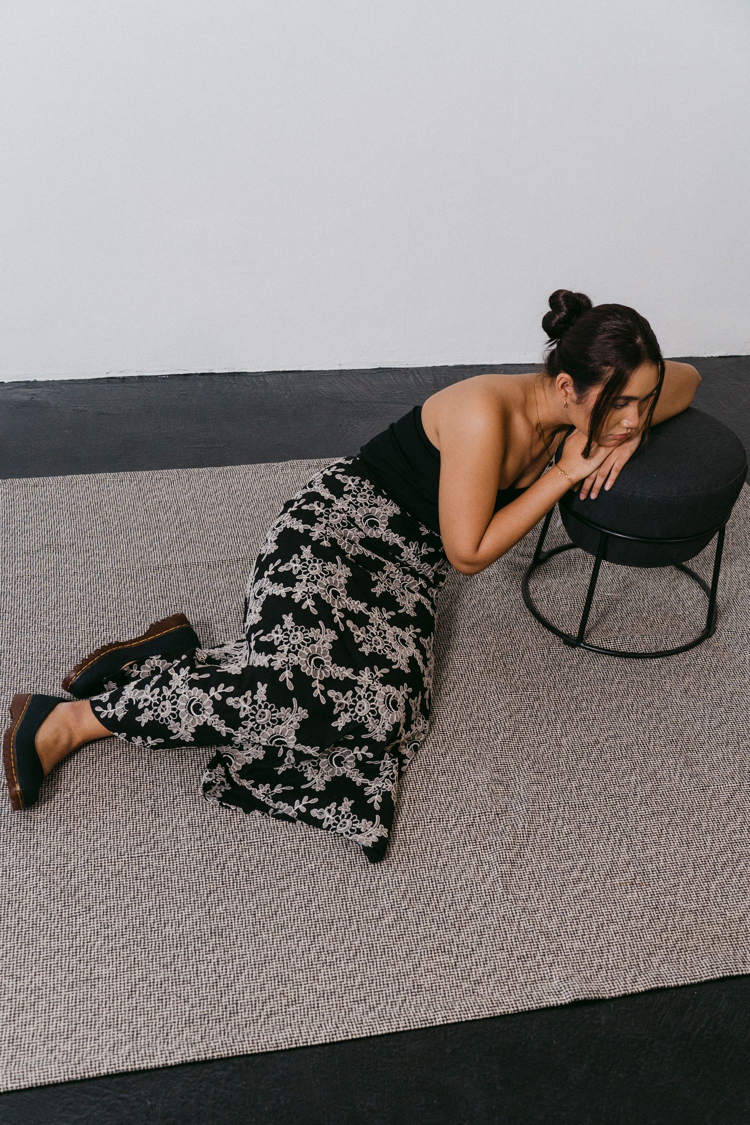Person in floral maxi dress rests on floor near modern chair in minimal setting.