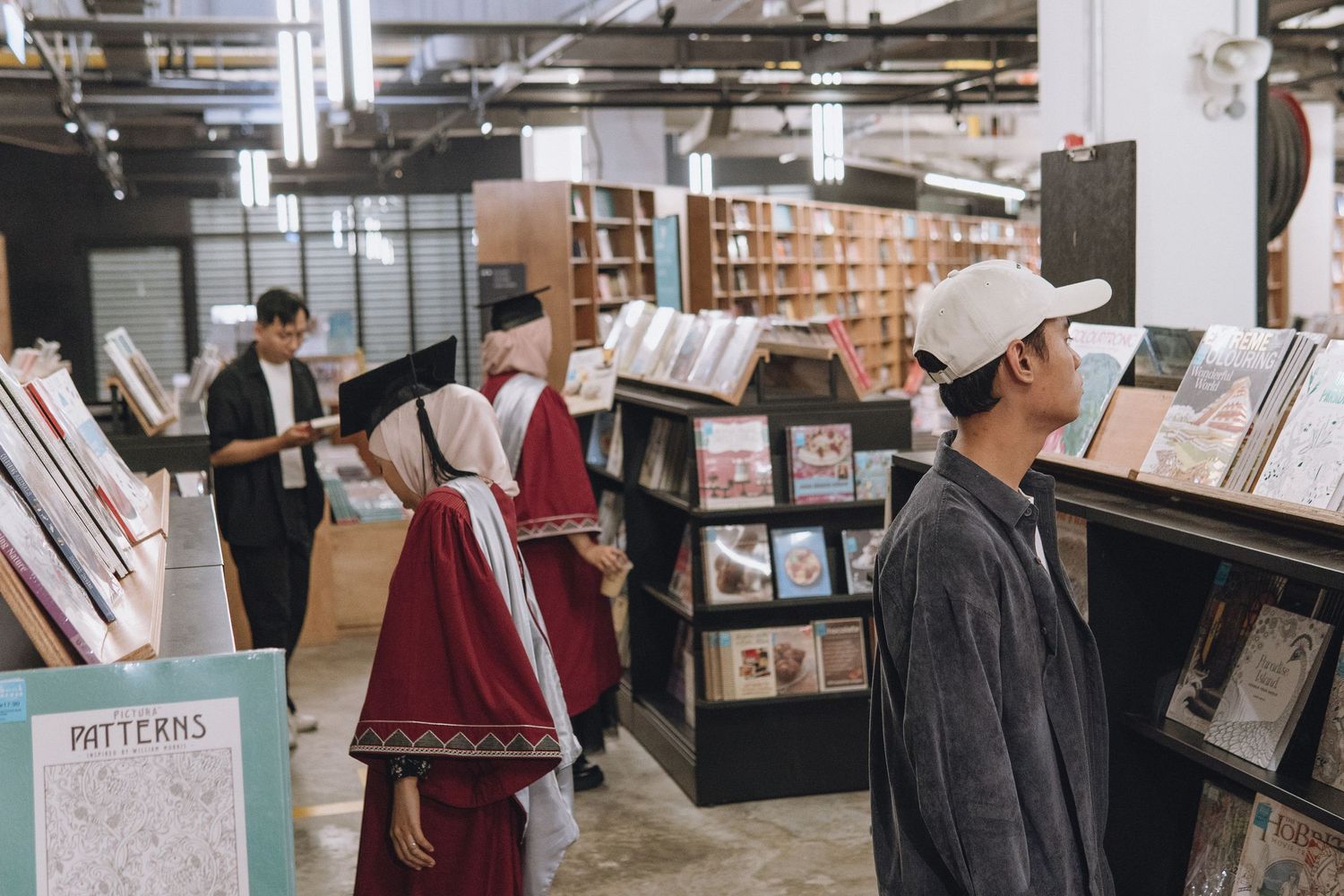 Students browse books in a modern library with industrial-style ceiling and dark shelving.