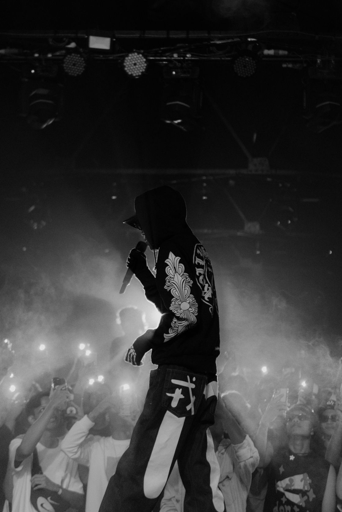 Silhouette of performer on stage with crowd and dramatic lighting in black and white.