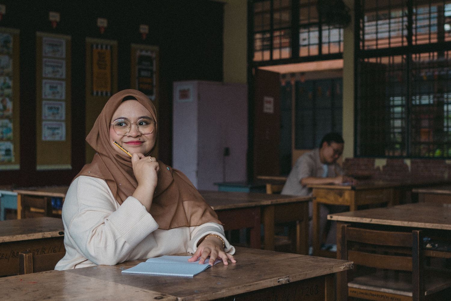Student sitting at desk in a traditional classroom with vintage furniture and decor.