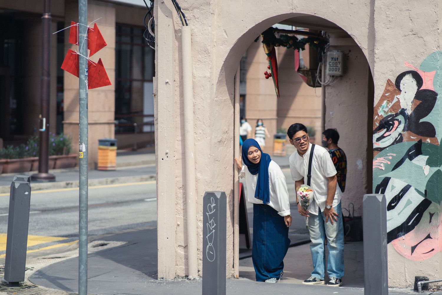 Two people stand under an arched doorway on a street with colorful murals and decorative elements.