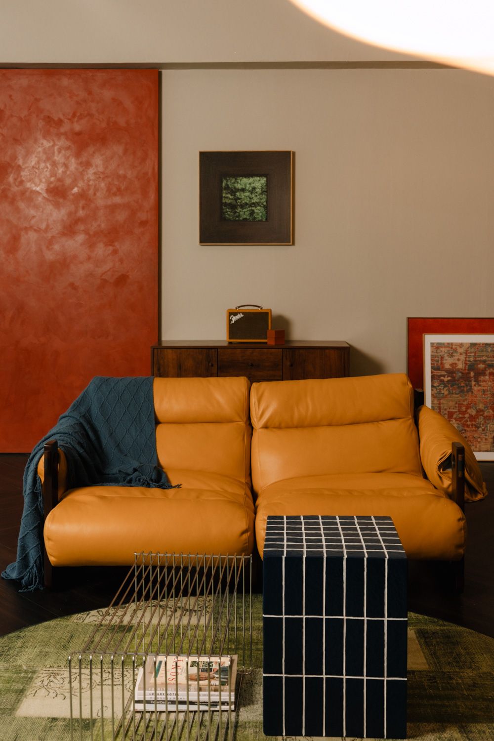 Mid-century modern living room with orange leather sofa, blue throw, geometric side table, and abstract wall art.