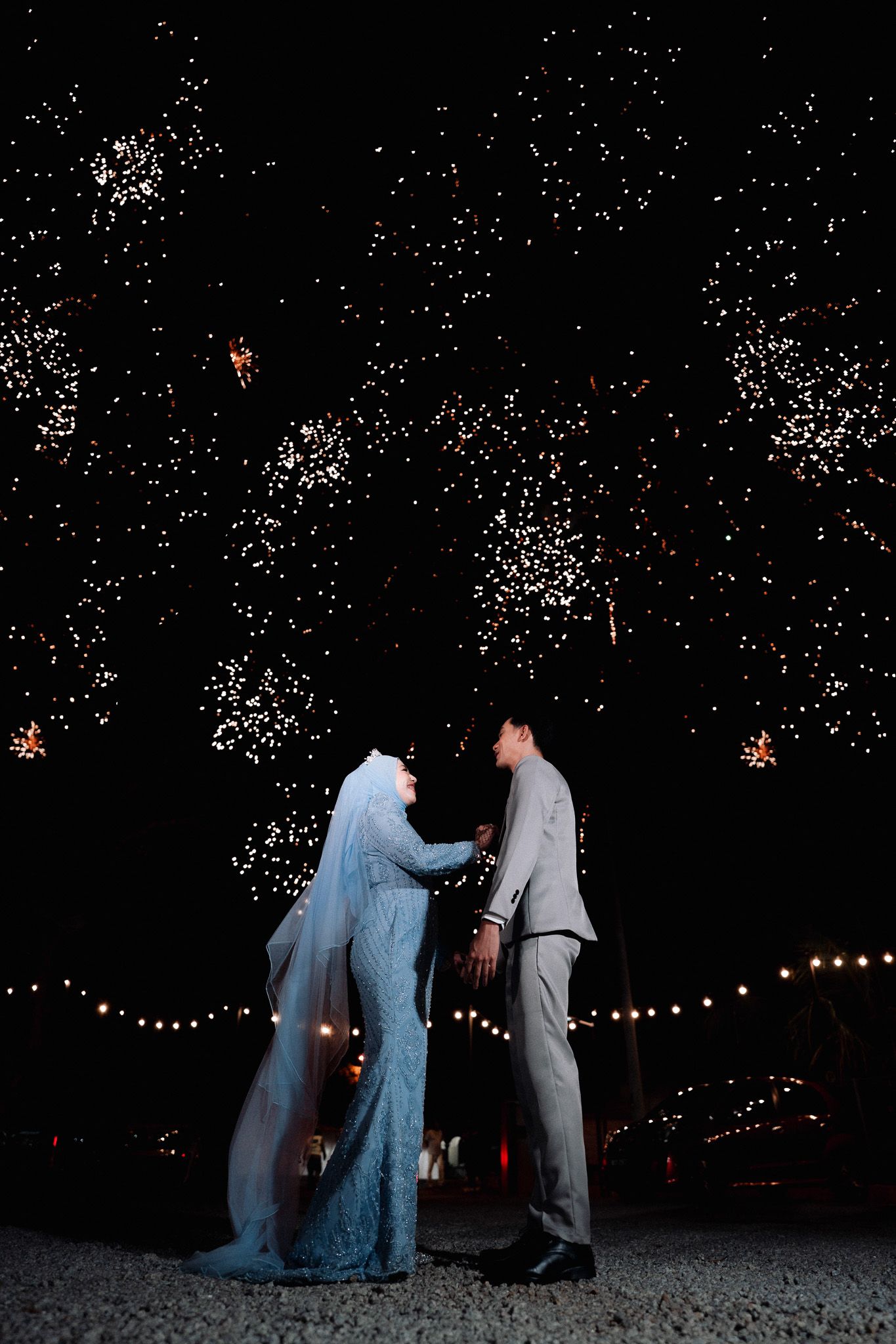 Bride and groom share a romantic moment under stunning fireworks display at night wedding celebration.
